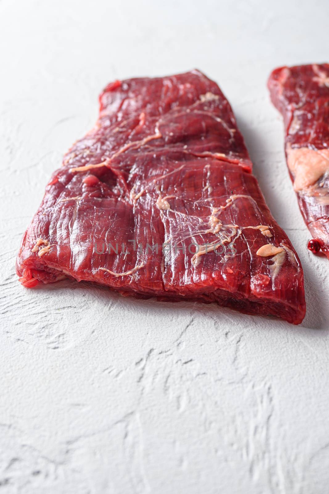 Raw Flap meat, London Broil organic meat cut side view close up over white concrete background vertical selective focus by Ilianesolenyi