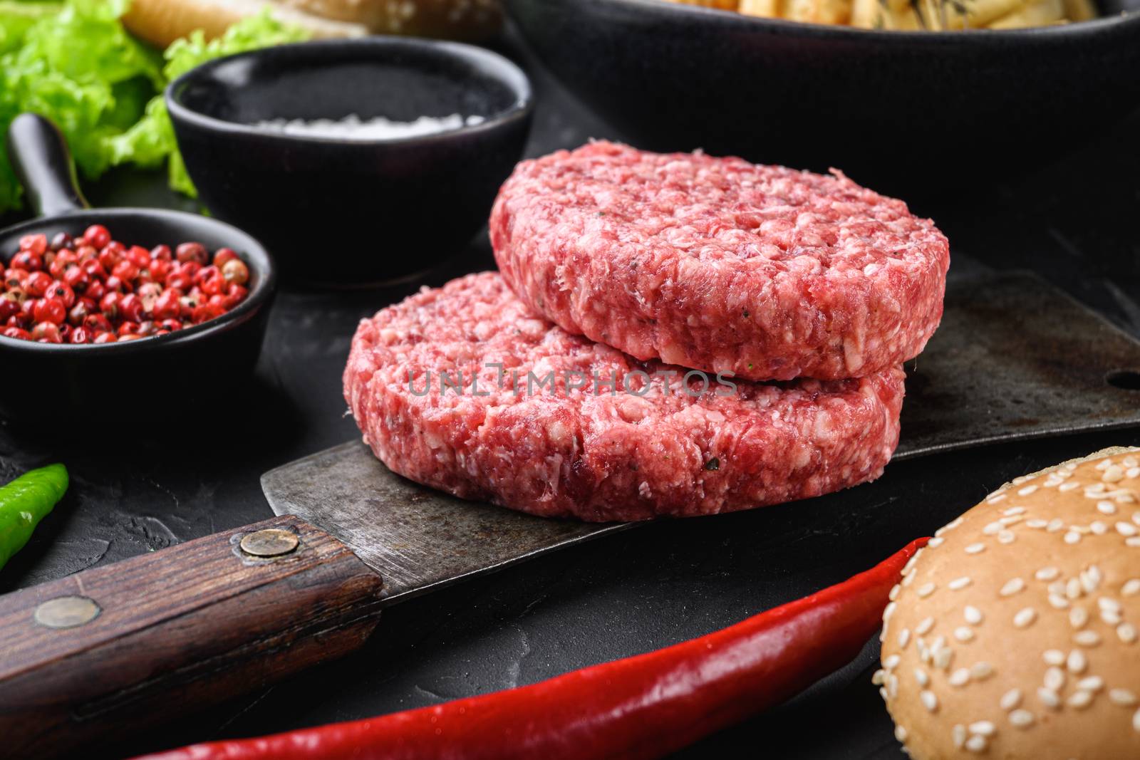 Raw ground beef cutlets with ingredients for burger on black background.