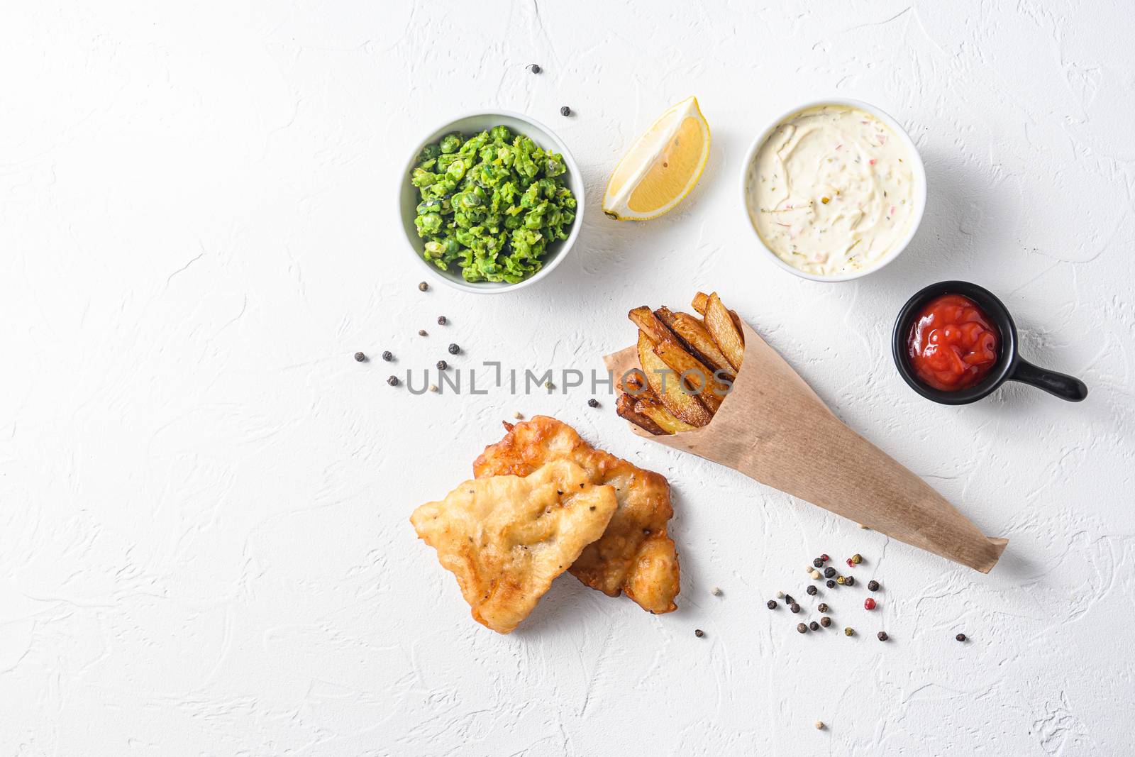 Fried fish and chips in a paper cone on white background with all components classic recipe takeaway food top view white stone textured background space for text.