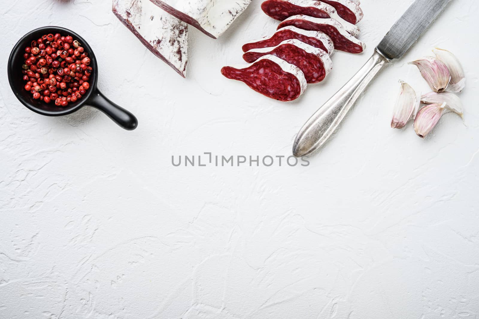 Sliced cuts of longaniza, dry cured spanish sausage with herbs and spices on white textured background with space for text.