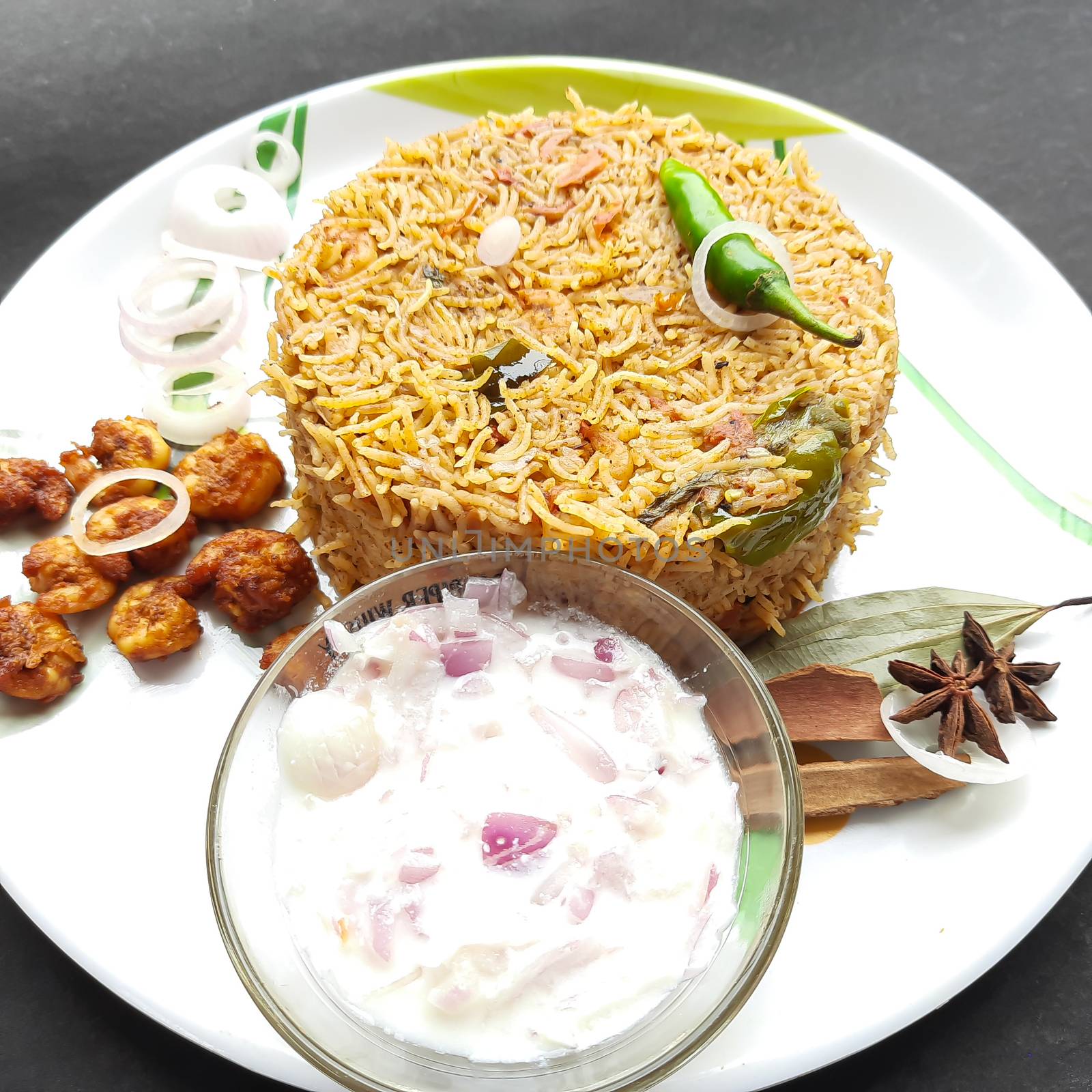 Colorful Delicious yummy prawn briyani with prawn fry in center with prawn fry and raita plated beautifully in white plate with bayleaf and it's one of favorite restaurant cuisine food