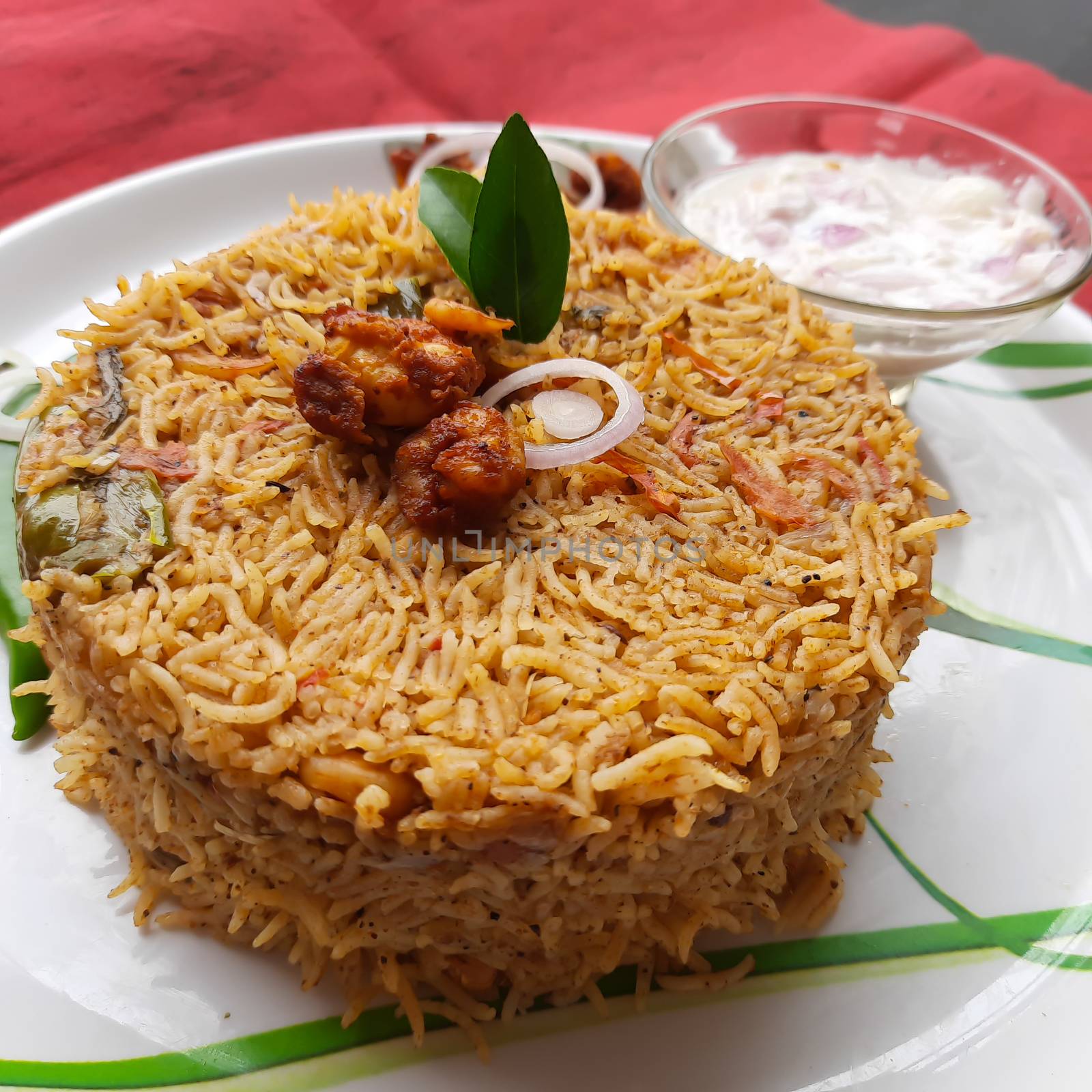 Colorful Delicious yummy prawn briyani with prawn fry in center with prawn fry and raita plated beautifully in white plate with bayleaf and it's one of favorite restaurant cuisine food by AnithaVikram