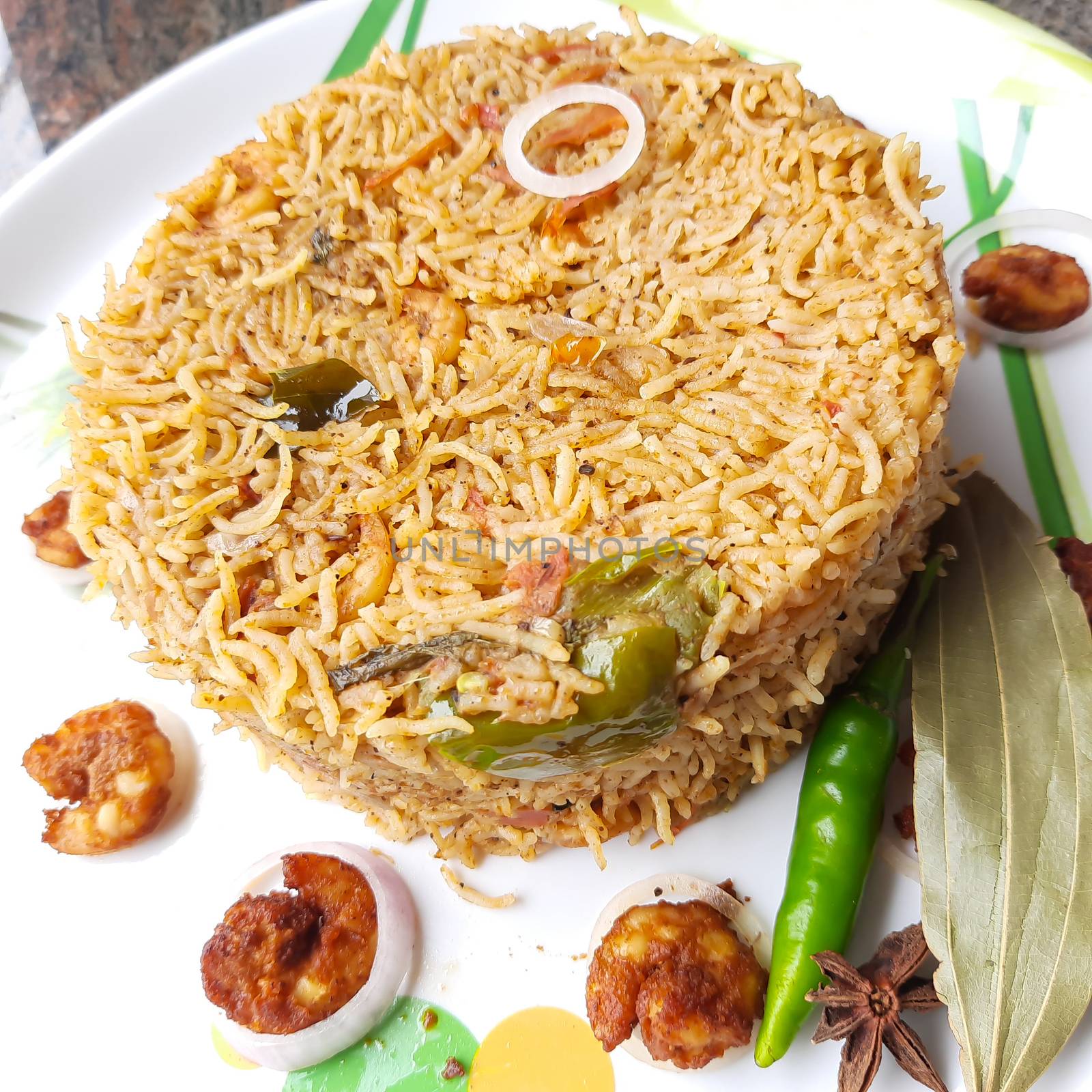 Colorful Delicious yummy prawn briyani with prawn fry in center with prawn fry and raita plated beautifully in white plate with bayleaf and it's one of favorite restaurant cuisine food