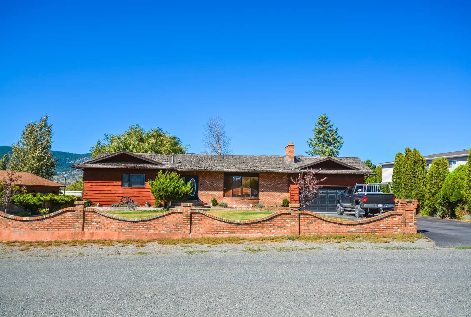 Red brick built residential house with red brick wall on front yard. Family house with black truck parked on asphalt driveway