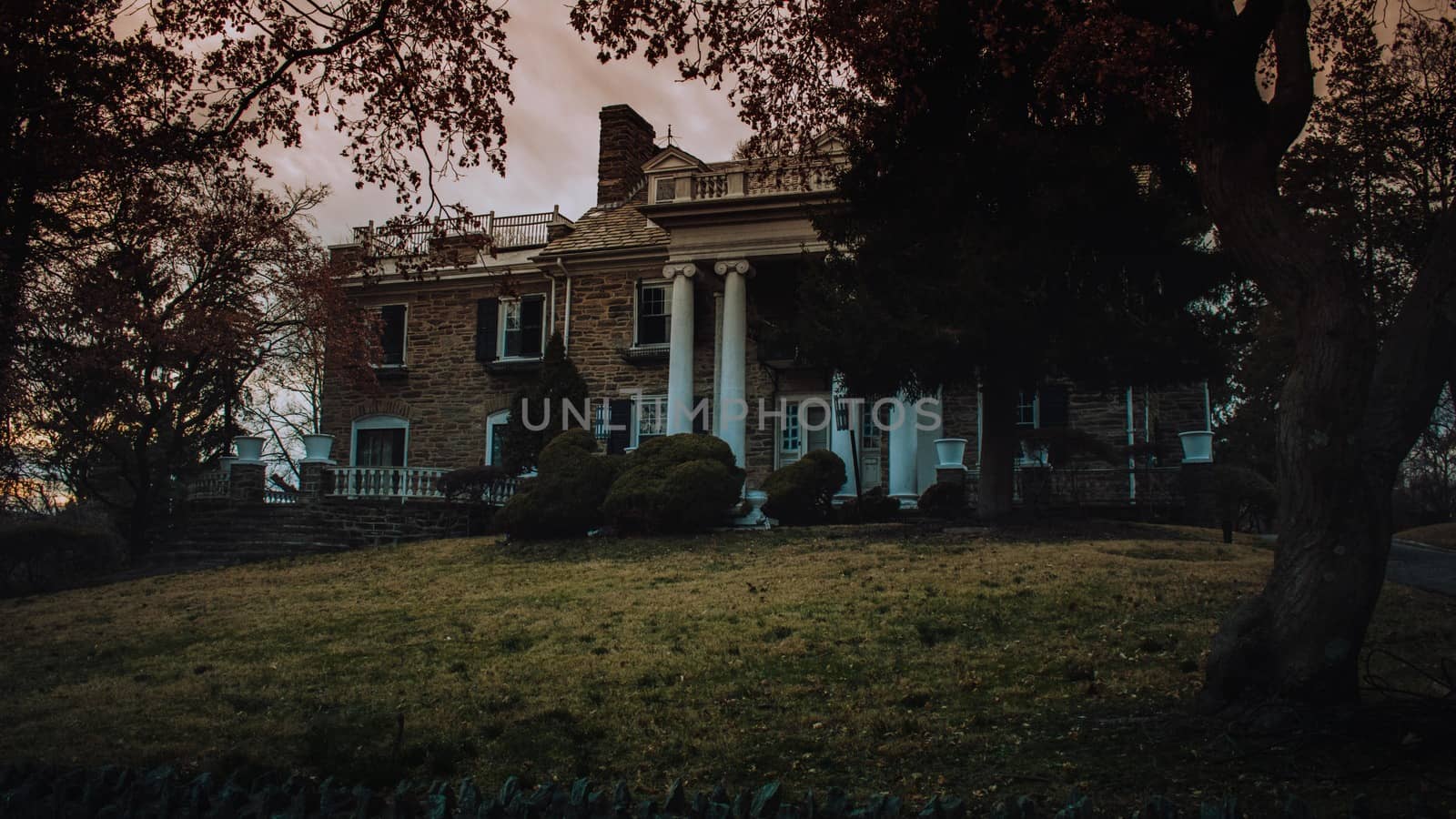 An Estate Like Building With a Large Front Yard, White Columns, and Trees Out Front