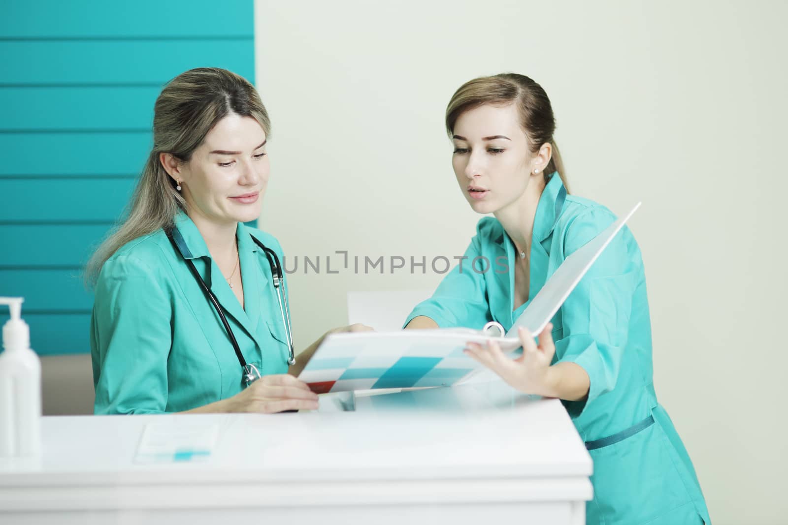 Two female doctor or nurse discussing patient treatment. Stethoscope phonendoscope on the neck. Holds a folder in his hands. Disinfectant on the table