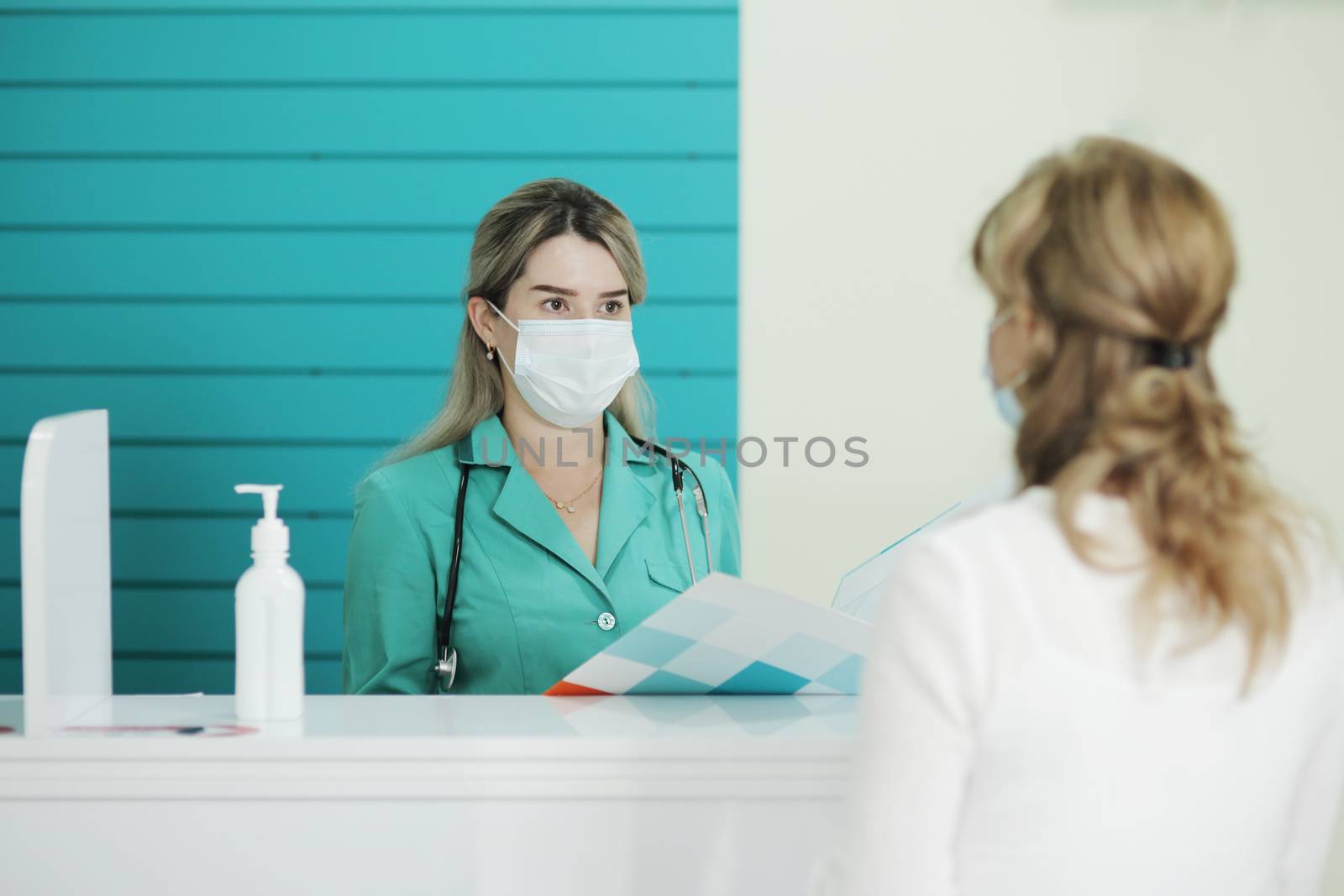 Woman doctor or nurse in a medical mask talks to a female patient by selinsmo