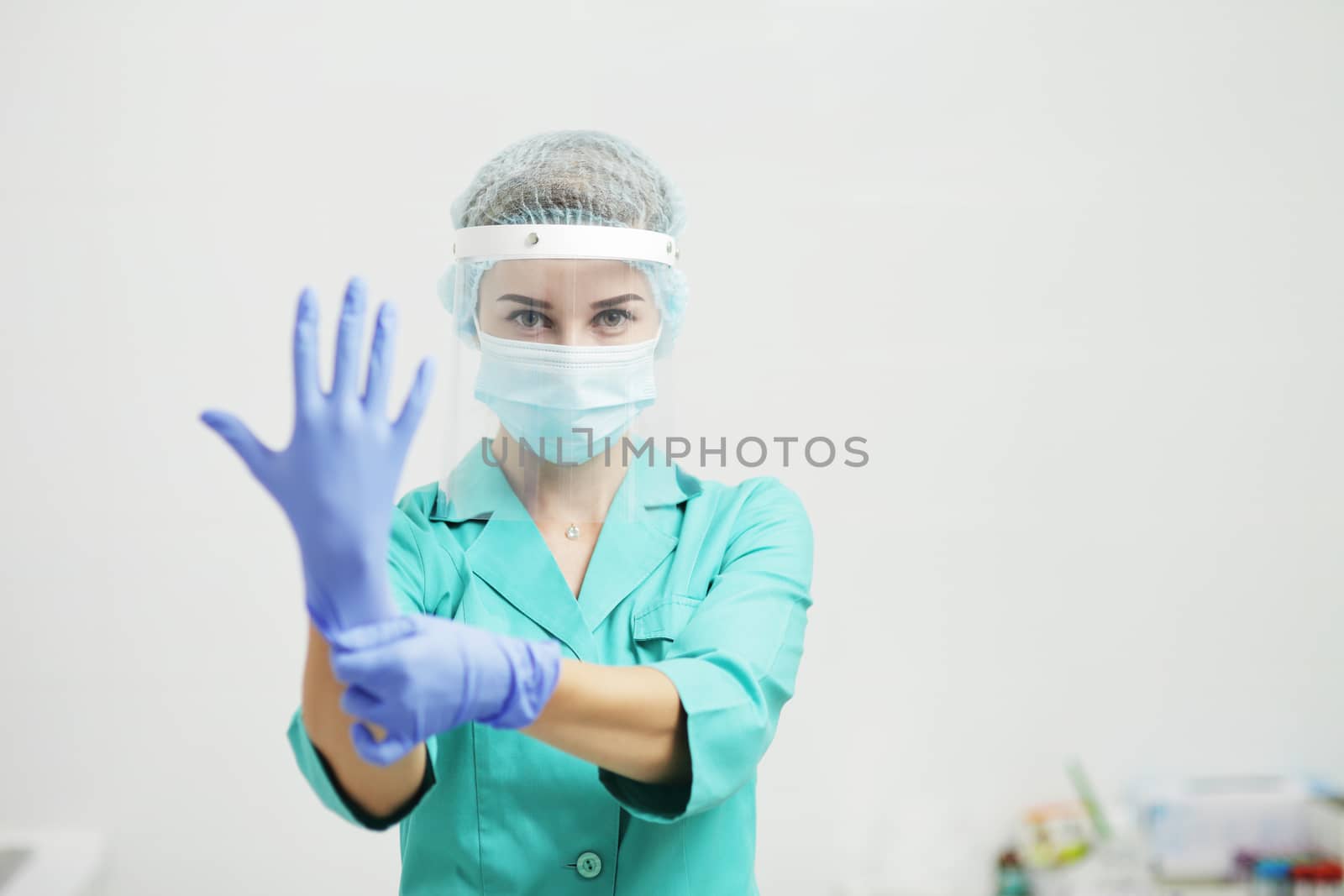 A woman doctor in uniform, medical mask, protective shield puts on gloves by selinsmo
