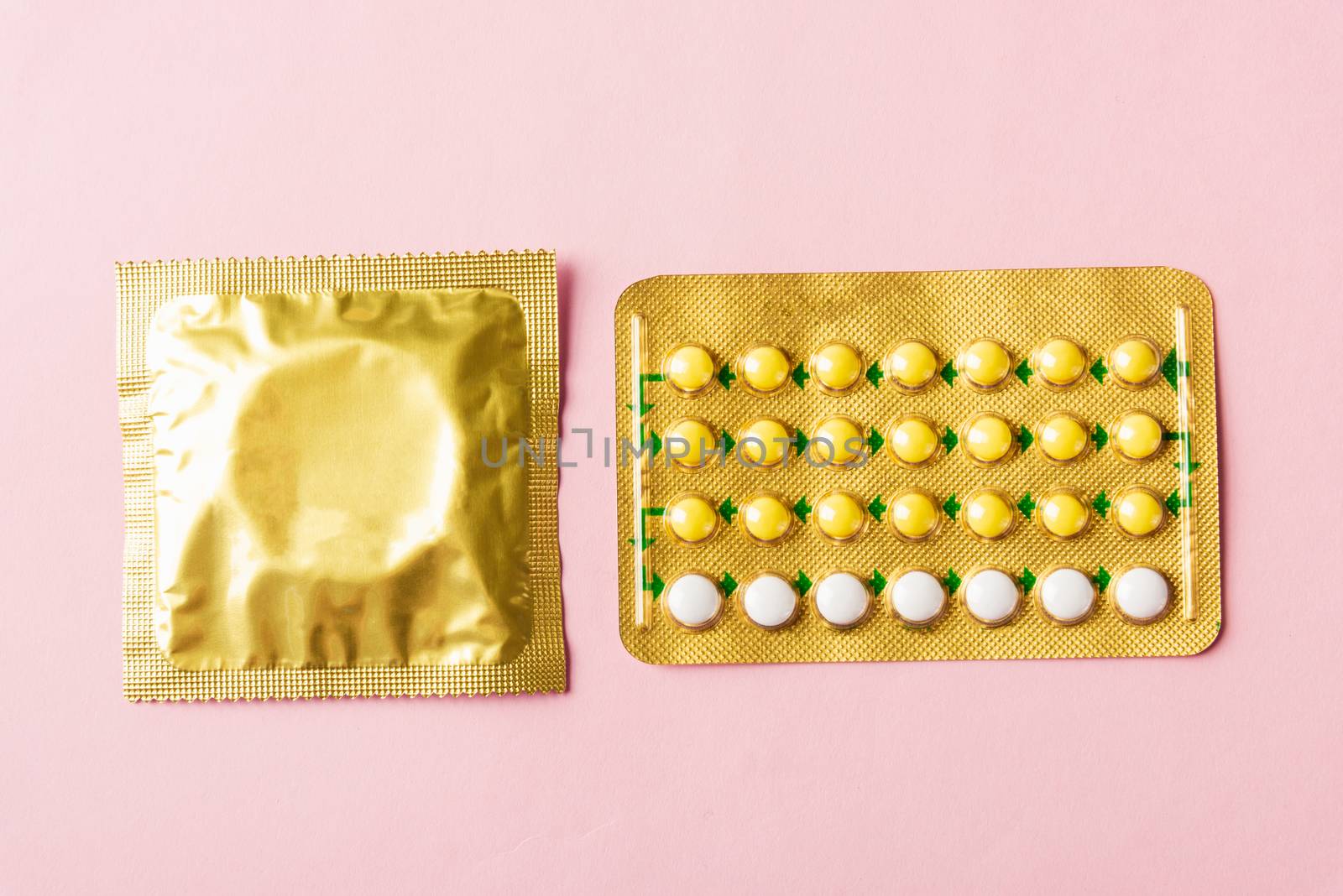 World sexual health or Aids day, condom in wrapper pack and contraceptive pills blister hormonal birth control pills, studio shot isolated on a pink background, Safe sex and reproductive health concept