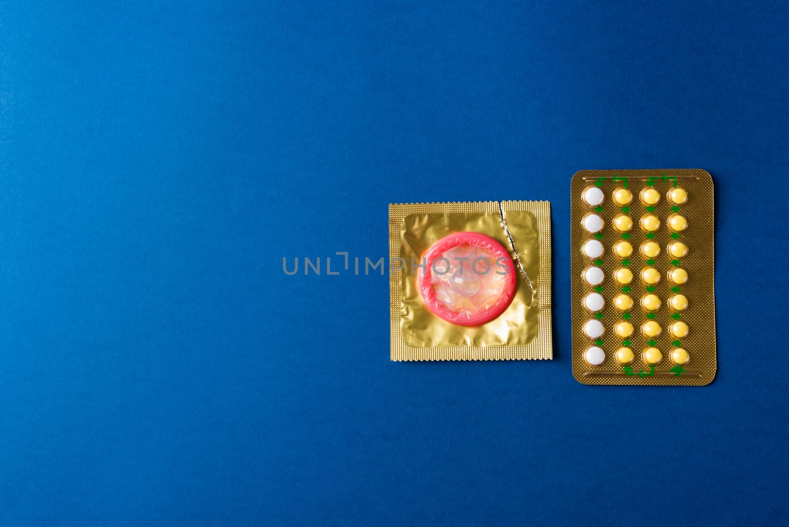 World sexual health or Aids day, condom on wrapper pack and contraceptive pills blister hormonal birth control pills, studio shot isolated on a dark blue background, Safe sex and reproductive health concept
