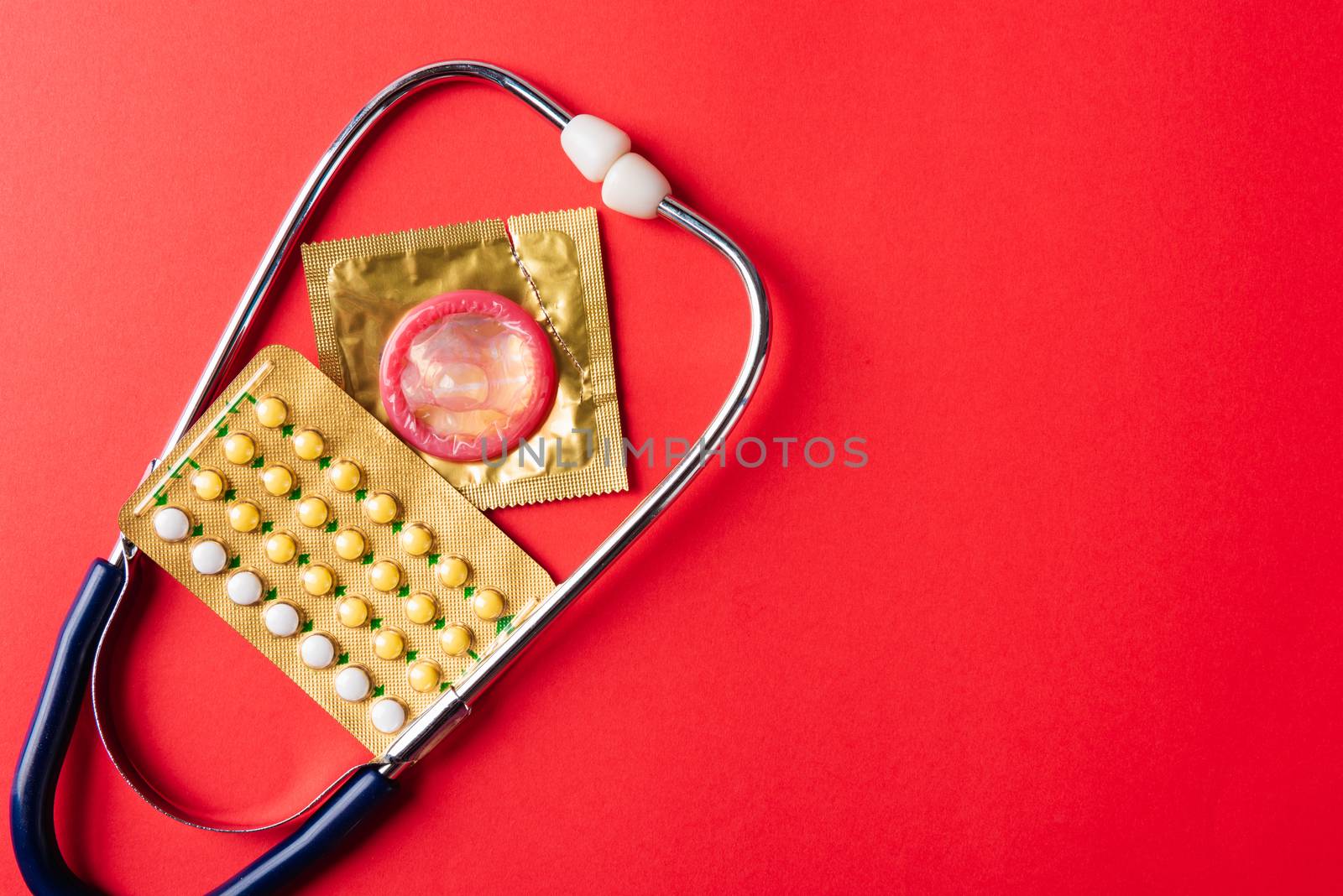 World sexual health or Aids day, Top view flat lay condom in wrapper pack, birth control pill and doctor stethoscope, studio shot isolated on a pink background, Safe sex and reproductive health concept