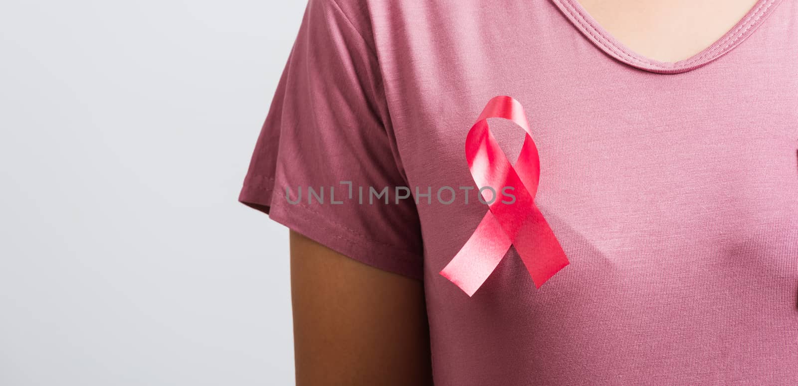 Breast cancer awareness healthcare and medicine concept. Close up Asian woman wear pink shirt standing with pink breast cancer awareness ribbon pin on chest, studio shot isolated on white background