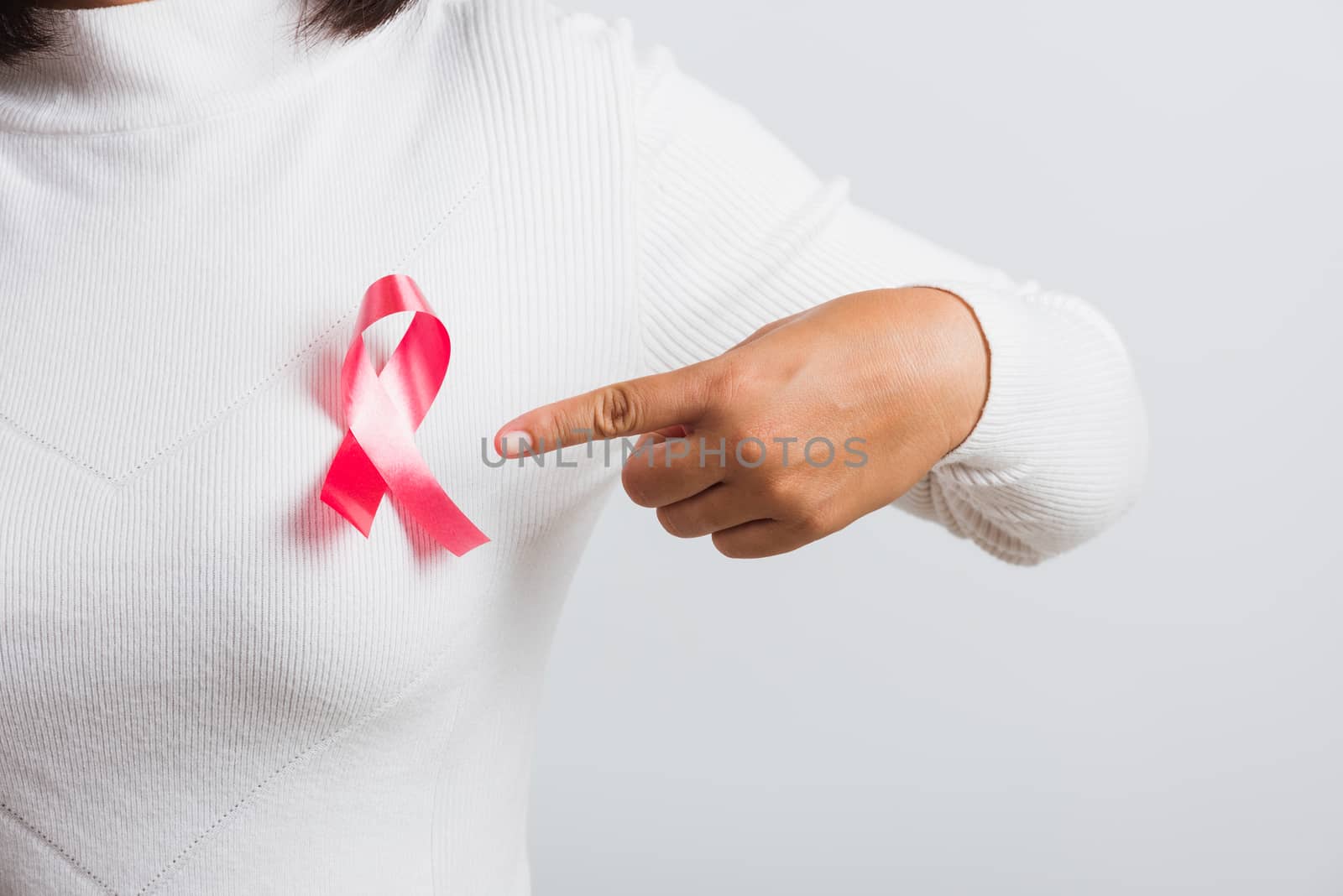 Breast cancer awareness healthcare and medicine concept. Close up Asian woman wear white shirt pointing finger to pink breast cancer awareness ribbon, studio shot isolated on white background