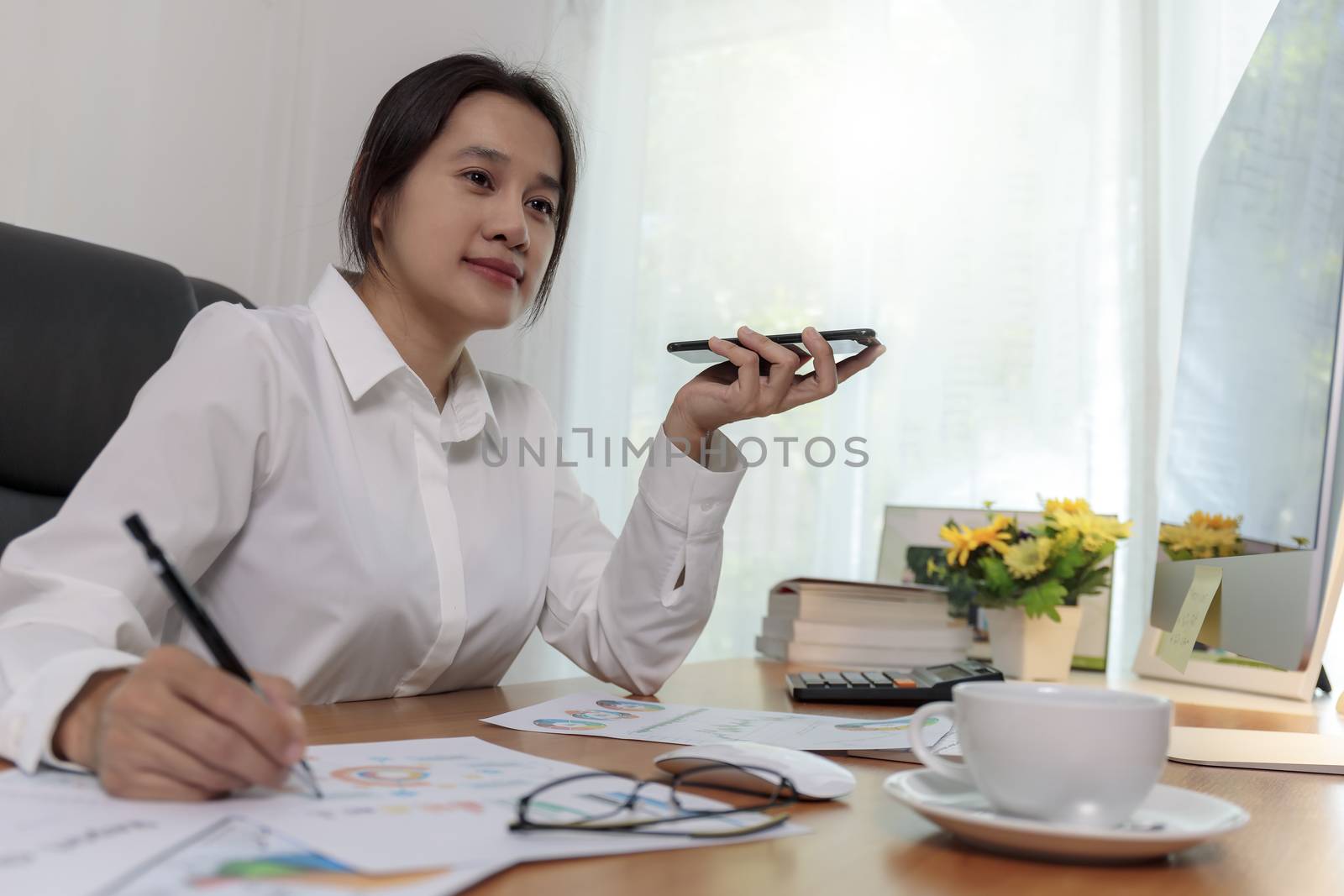 Business women holding smart phone to speak with speaker phone and taking write notes on desk at office. Business people call for working with customer or partner with smart phone. Business concept.