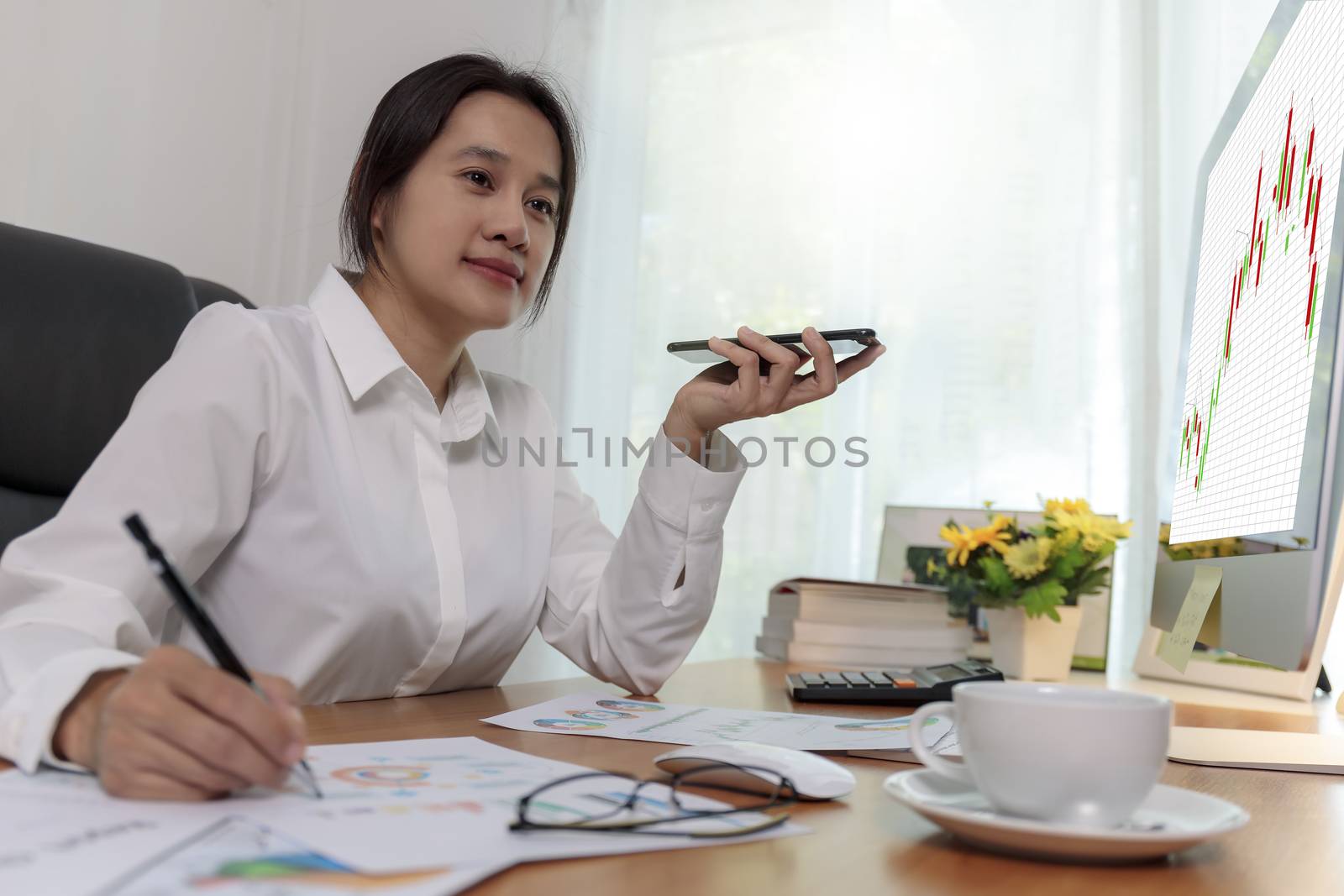 Business women holding smart phone to speak with speaker phone and taking write notes on desk at office. Business people call for working with customer or partner with smart phone. Business concept.