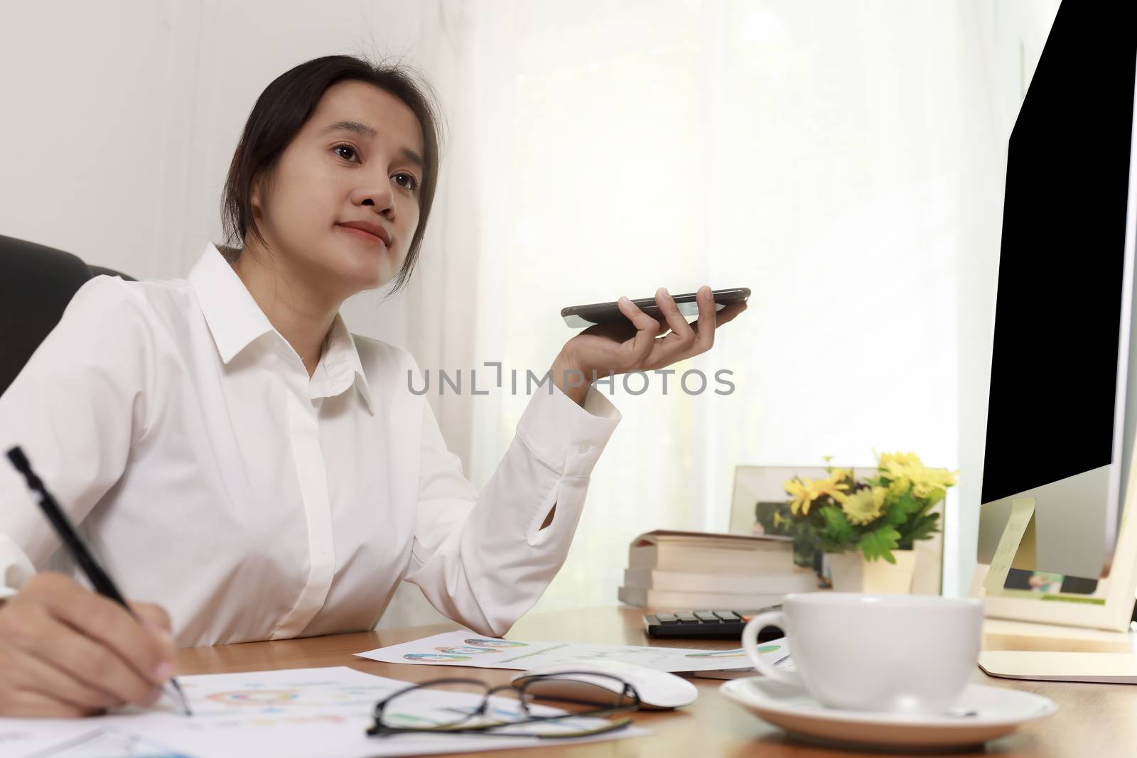 Business women holding smart phone to speak with speaker phone and taking write notes on desk at office. Business people call for working with customer or partner with smart phone. Business concept.
