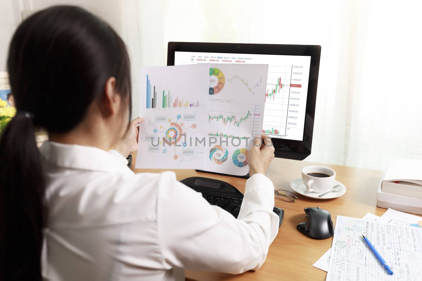 Rear view of business woman working in office with computer holding chart report paper and looking. business people working at home with paper and PC screen. Business and finance ,work at home concept