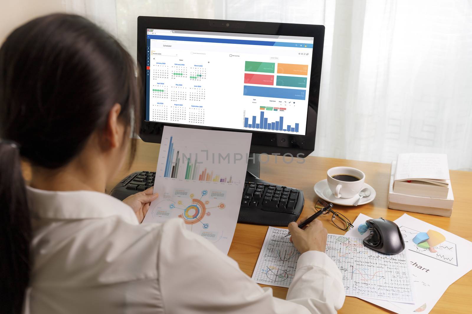 Rear view businesswoman working in office with computer holding chart report paper and looking. businesswoman analysis scheduler data on PC screen. Business people check calendar planner organisation