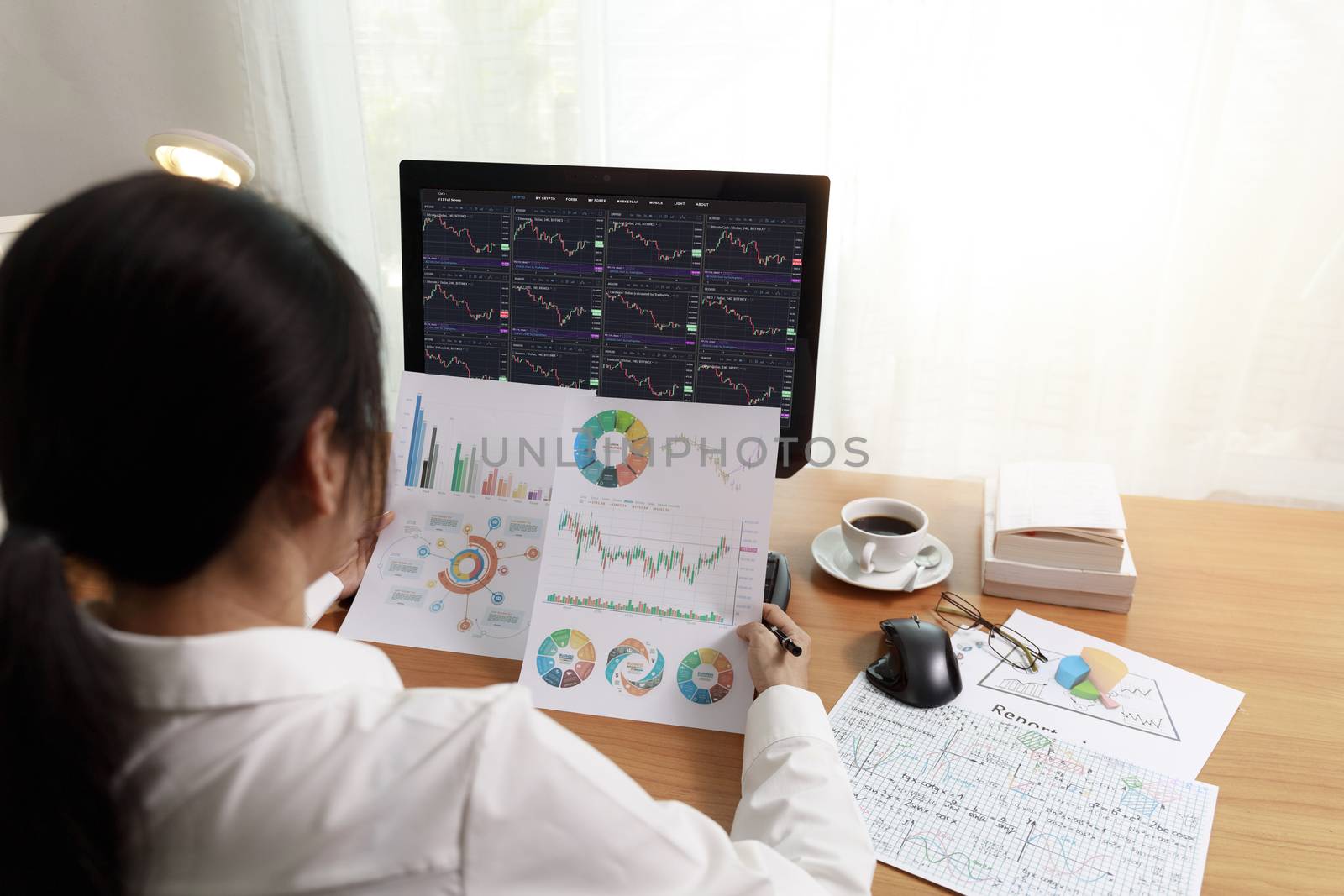 Rear view business woman working in office with computer holding chart report paper and looking. business people analysis stock market, forex chart data on PC screen and paper. Business and finance concept.