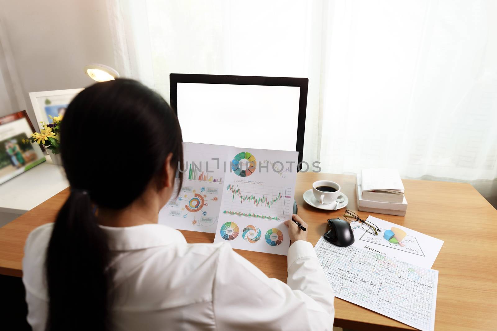 Rear view of businesswoman working in office with computer holding chart report paper and looking. businesswoman working at home with paper and empty PC screen. Business and finance concept.