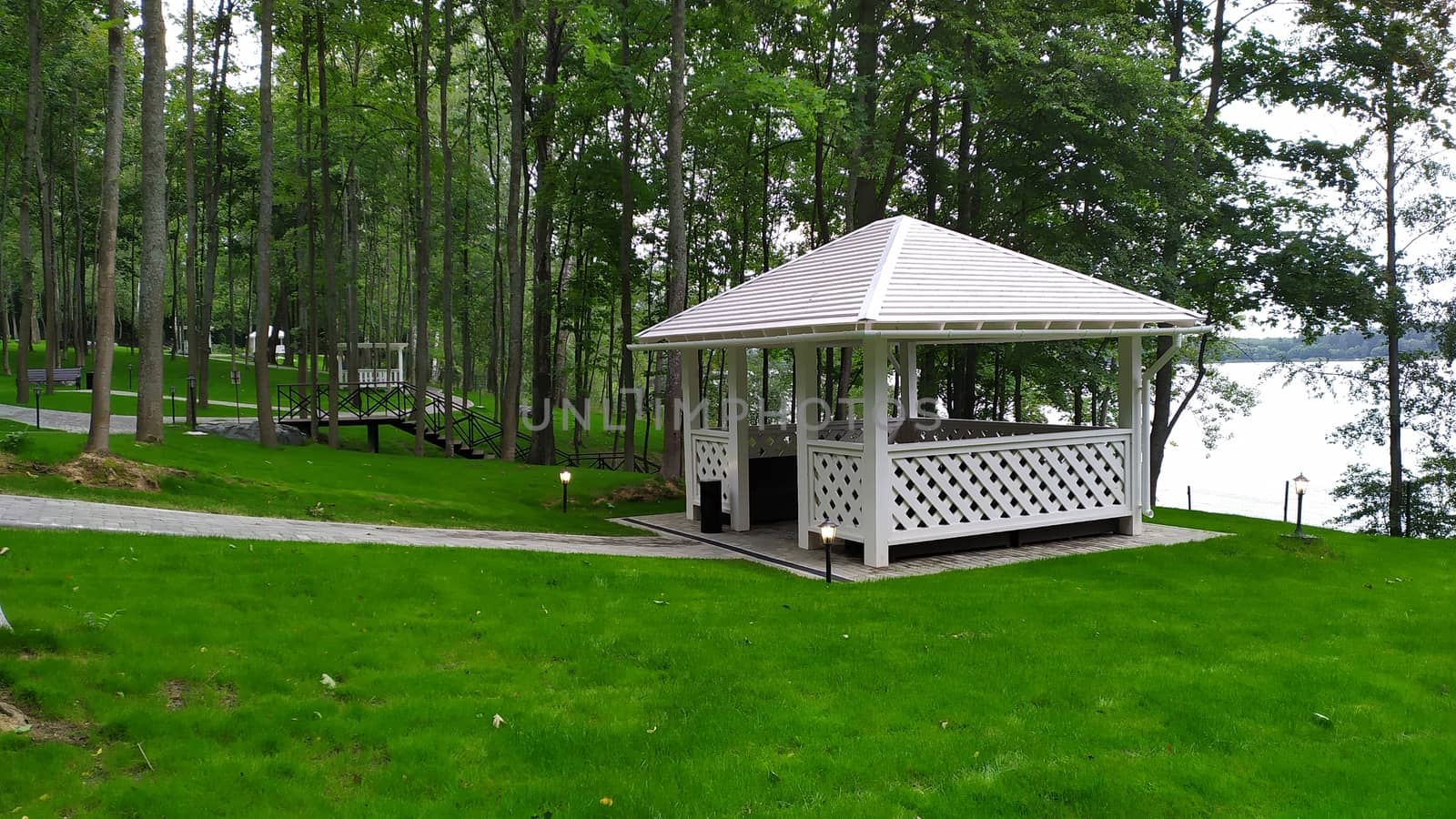 White gazebo in forest with trimmed lawn by marynkin