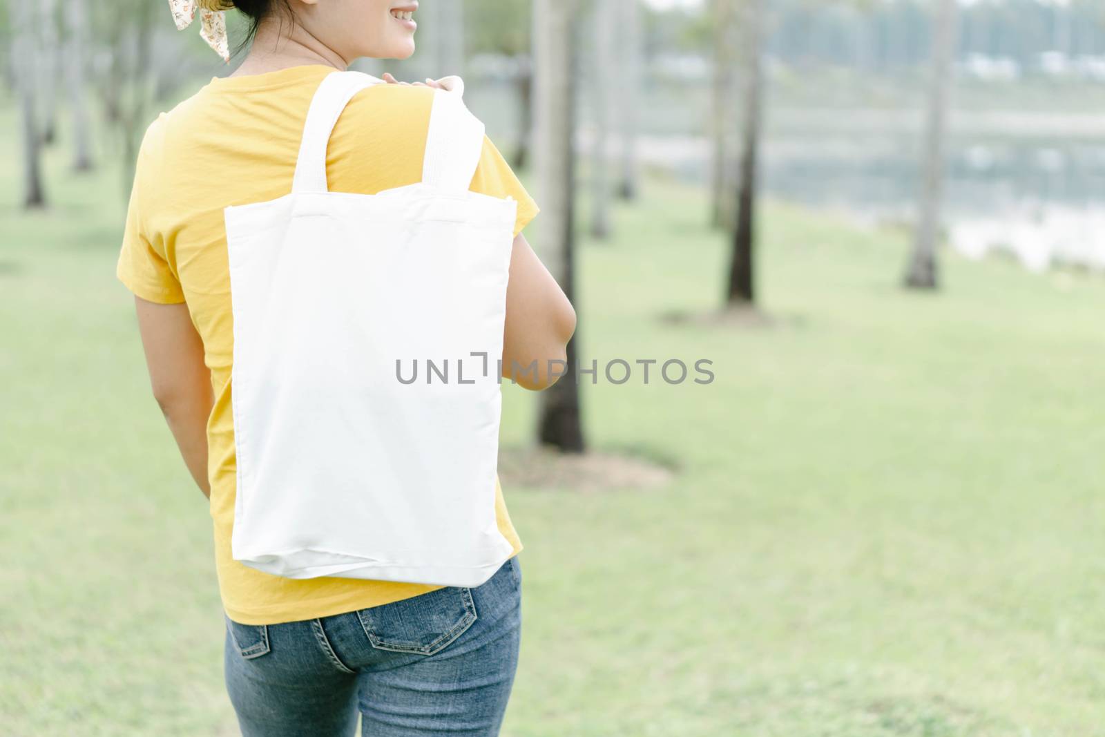 Closeup woman hand holding white bag canvas fabric on green nature background, Save the world concept