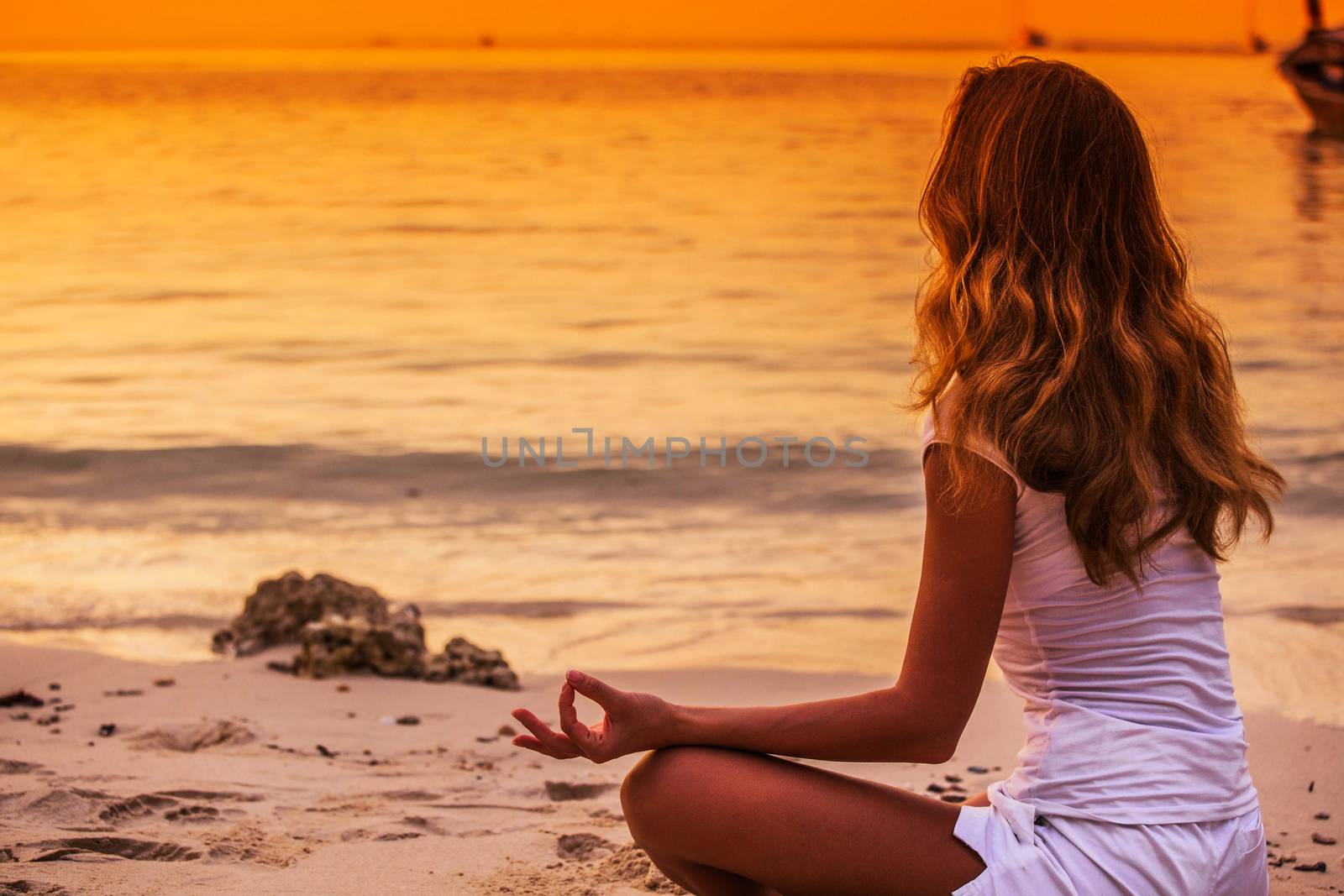 Yoga woman in lotus pose on sea coast at sunset