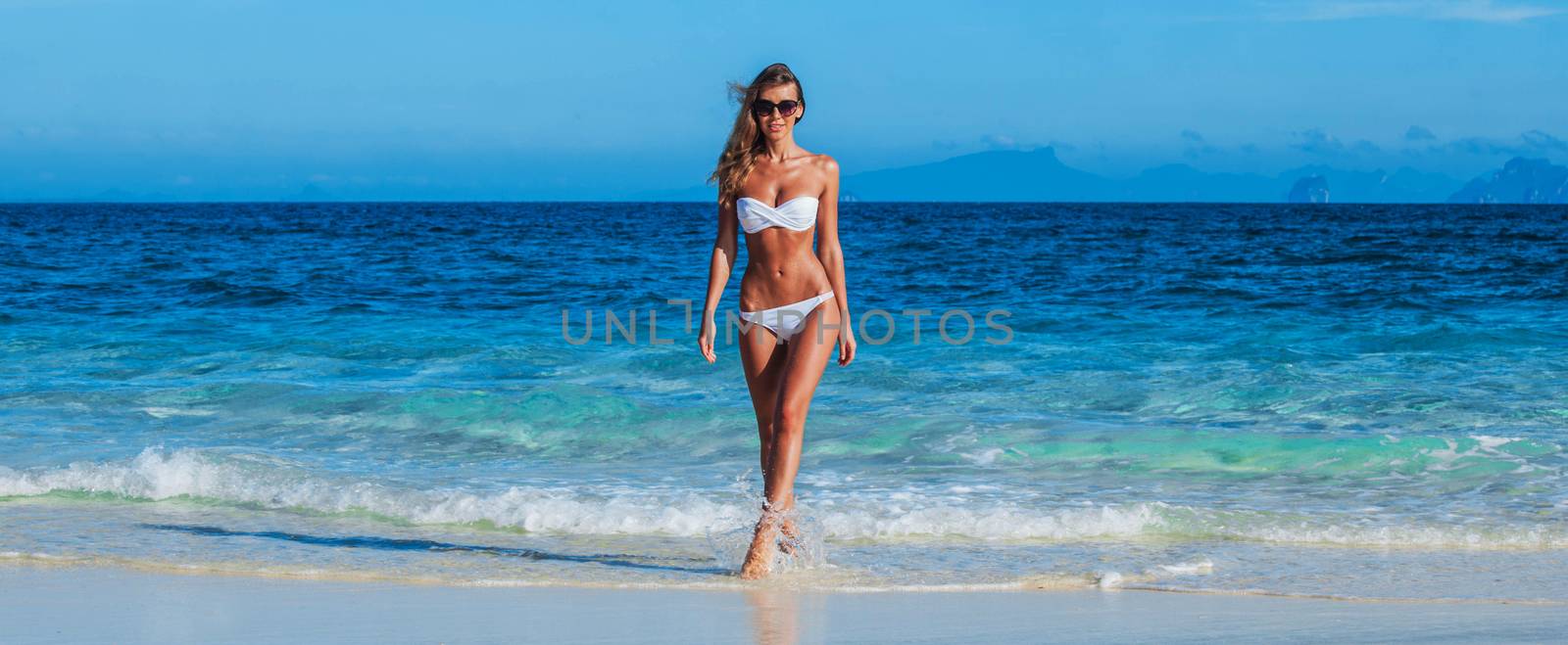 Pretty smiling girl in bikini walking in transparent water of tropical sea