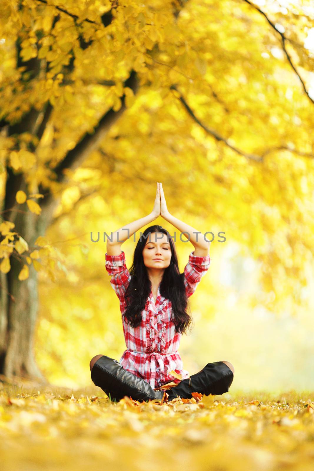 Beautiful young woman sitting in lotus yoga position in autumn park
