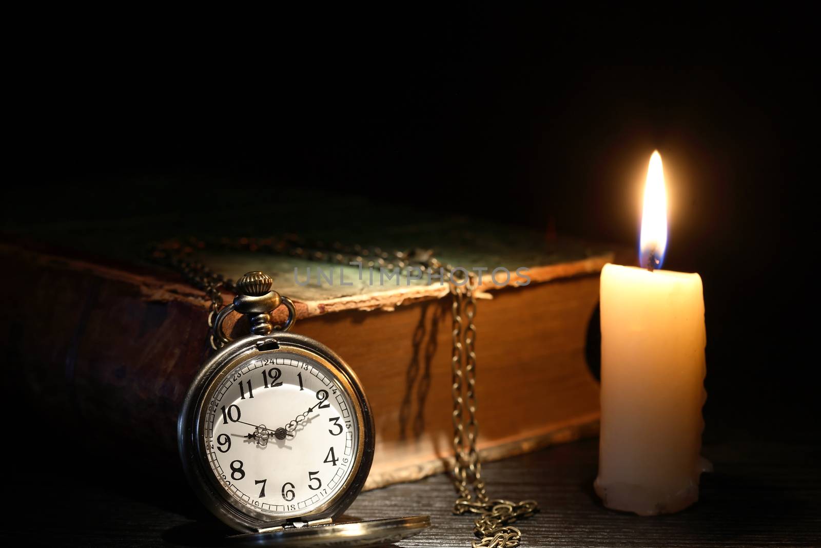 Old pocket watch near old book and candle on dark background