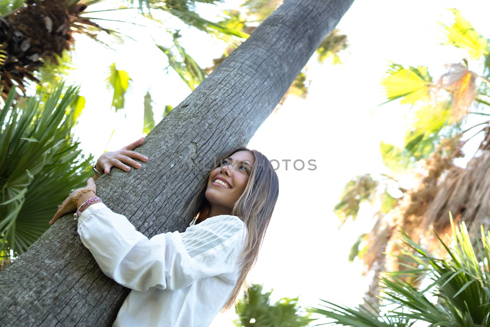 Young beautiful caucasian woman embracing a tree trunk in a green forest - Smiling girl hugging a palm - Save and protect the nature concept by robbyfontanesi