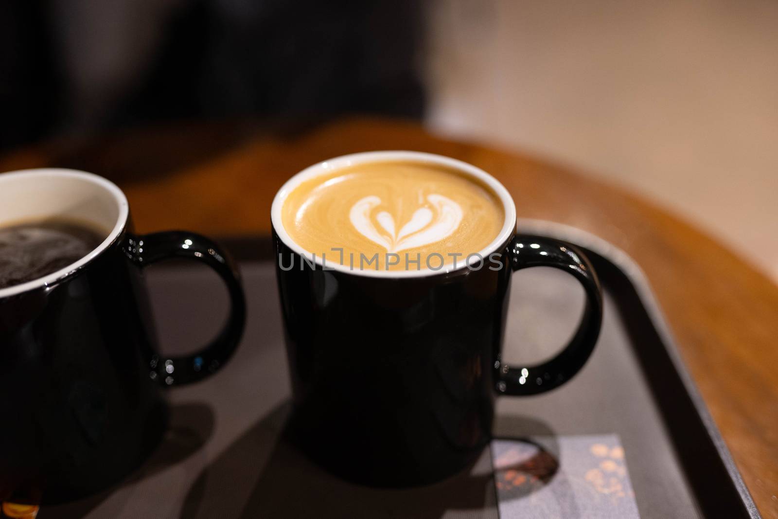 Two cups of coffee with latte art on black tray