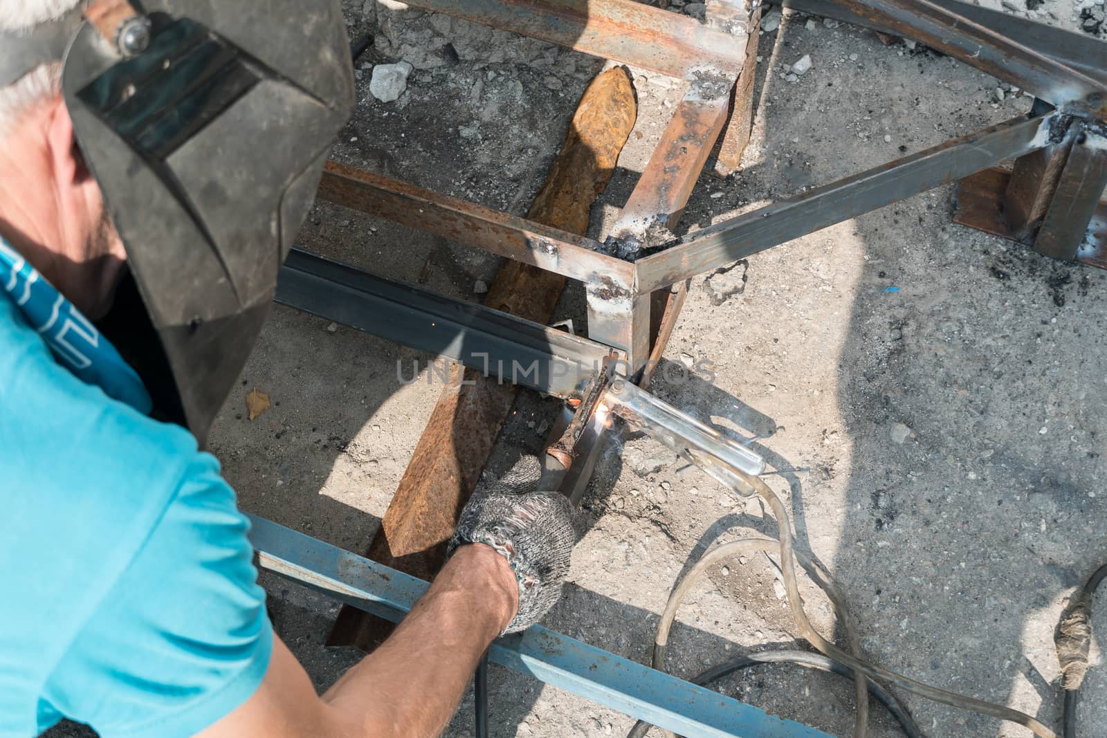 A working welder builds or repairs a new porch and facade of a building or structure. Construction and repair work on the street outdoor. Welder welds metal structure. Construction worker at work