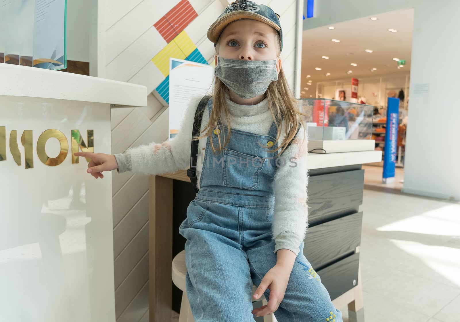 A baby girl wearing a protective medical mask at a shopping Mall during a coronavirus quarantine.
