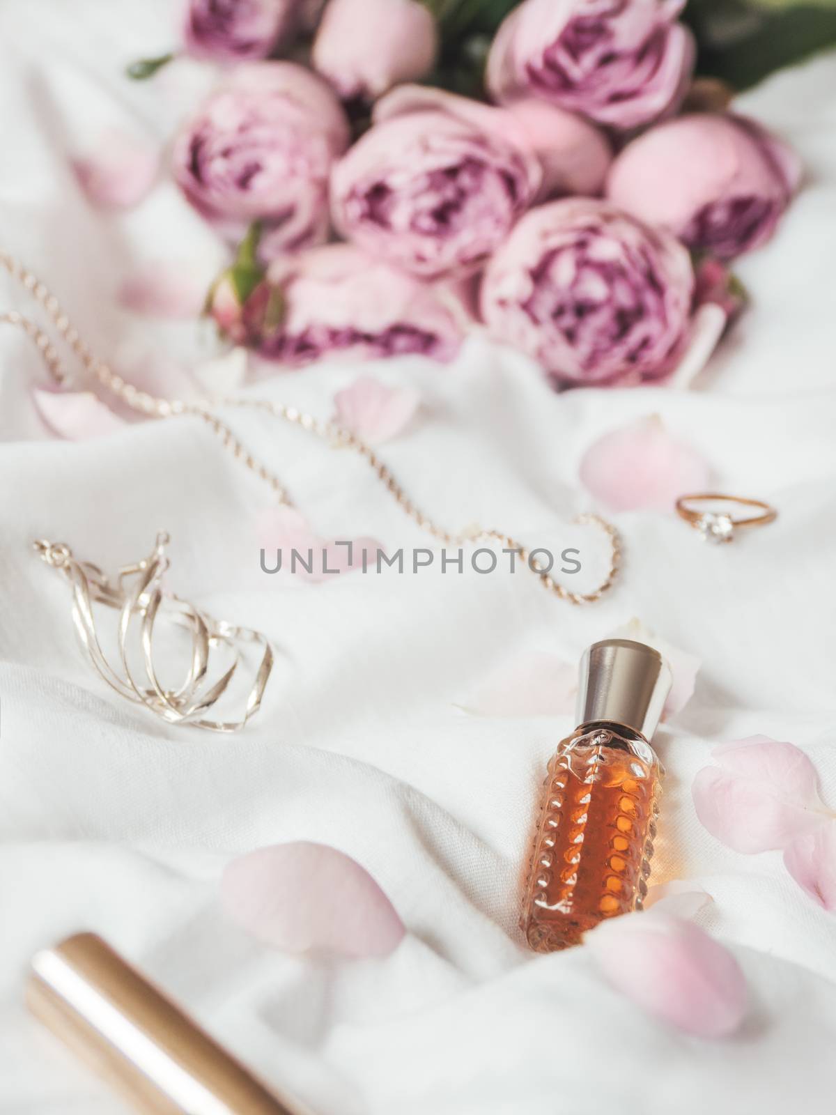 Pink roses and petals on crumpled white fabric background. Decorative cosmetic - perfume, mascara. Cute and fashionable jewelry accessories.