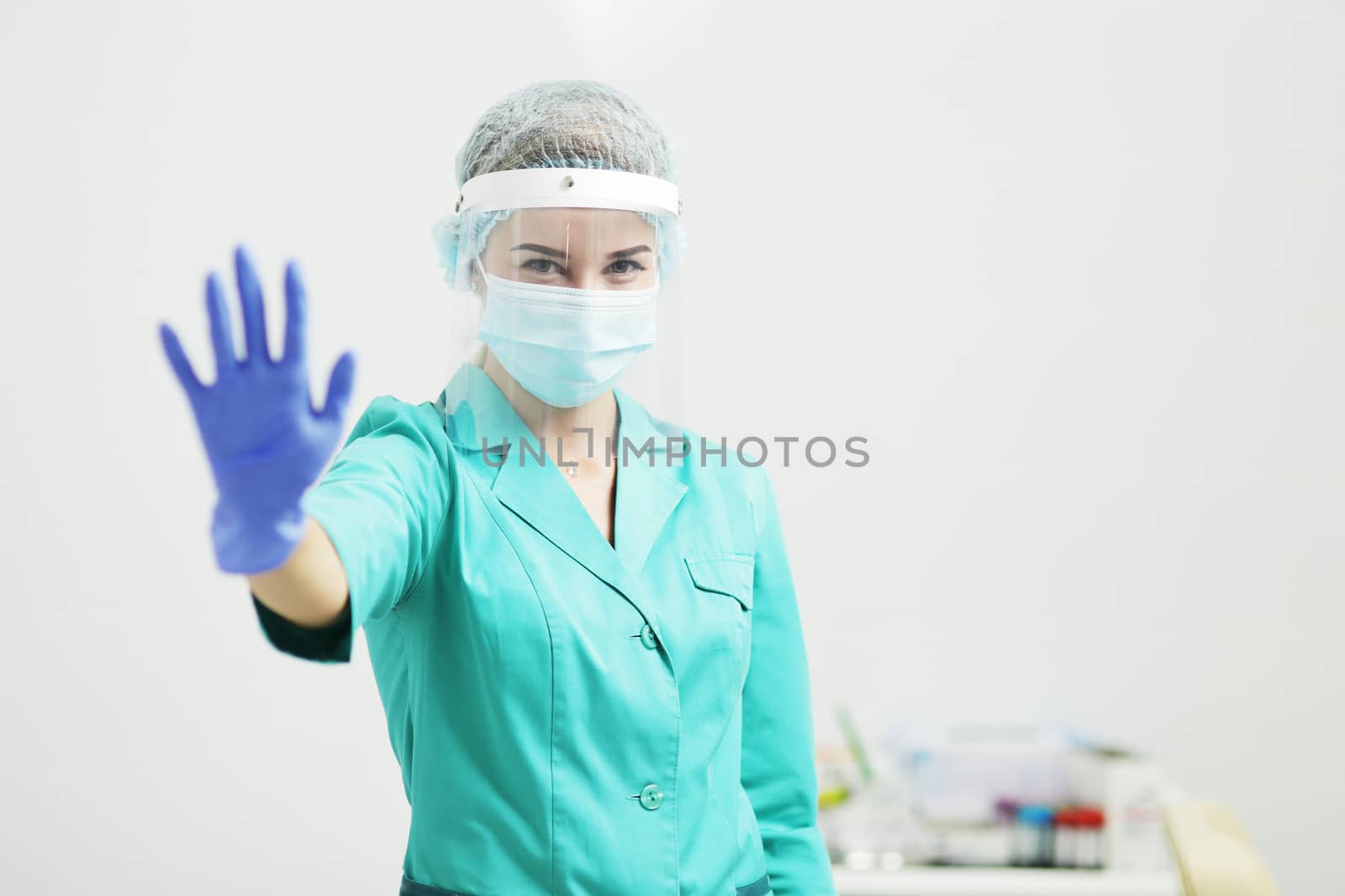 A woman doctor in uniform, medical mask, protective shield, gloves. Stop gesture by selinsmo