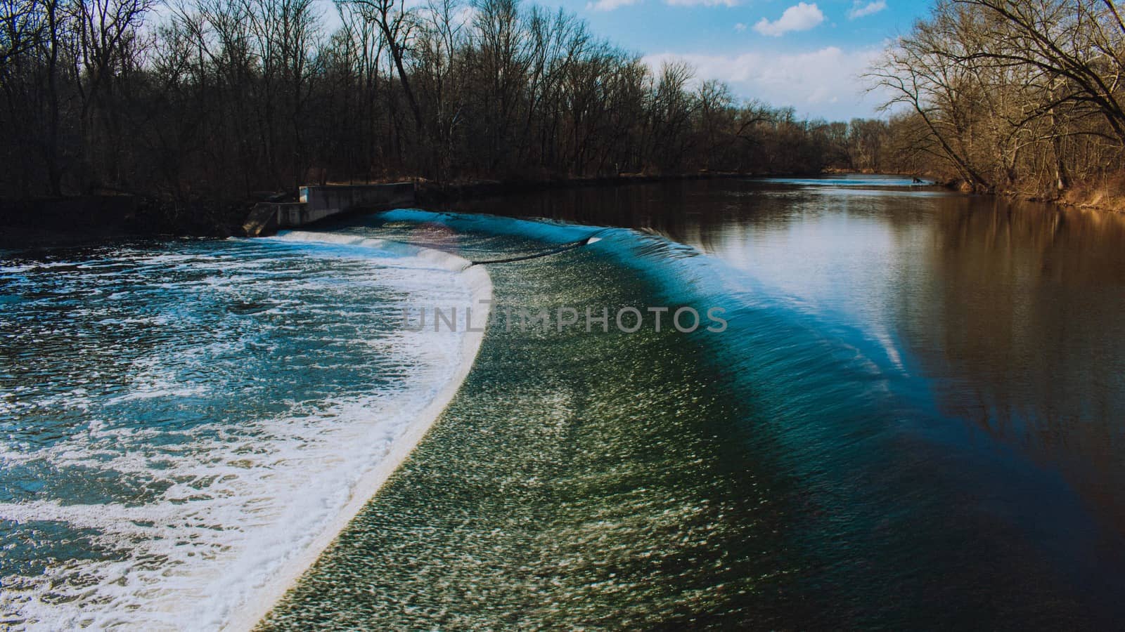 Fast Flowing Water Crashing Over a Man-Made Dam in a Winter Fore by bju12290