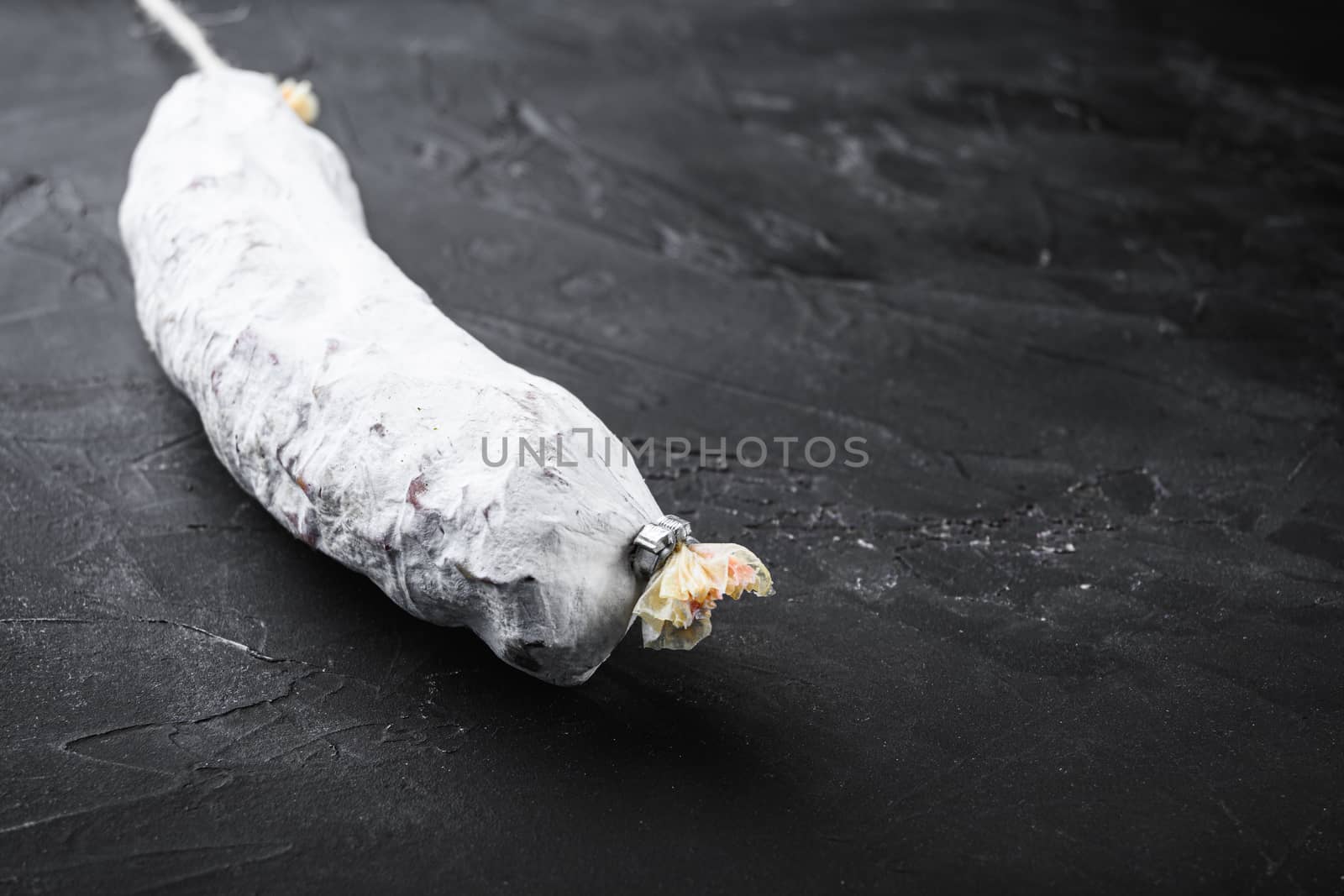 Spanish salchichon dry cured sausage on black surface with copy space.