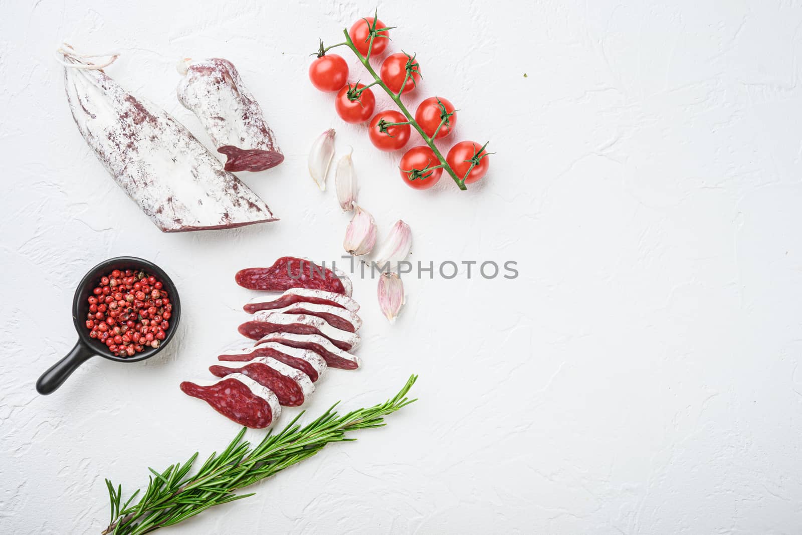 Sliced cuts of longaniza, dry cured spanish sausage with herbs and spices on white textured background, topview with space for text.
