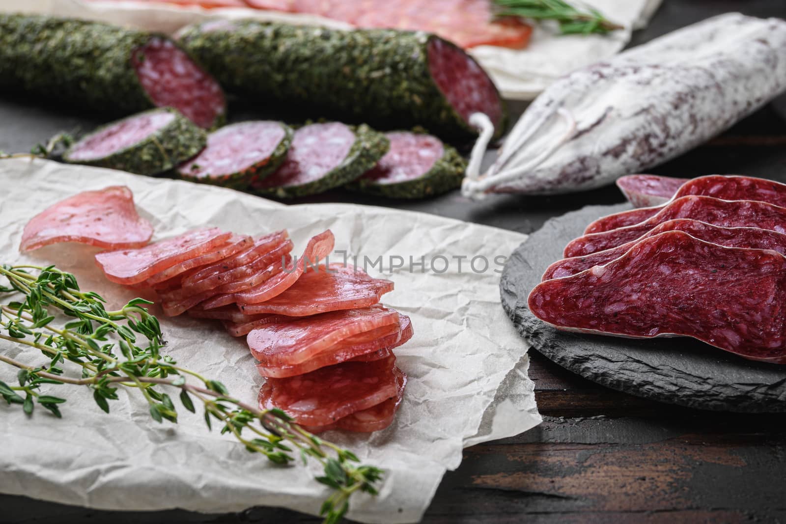 Variety of dry cured chorizo, fuet and other sausages cut in slices with herbs on dark wooden background.