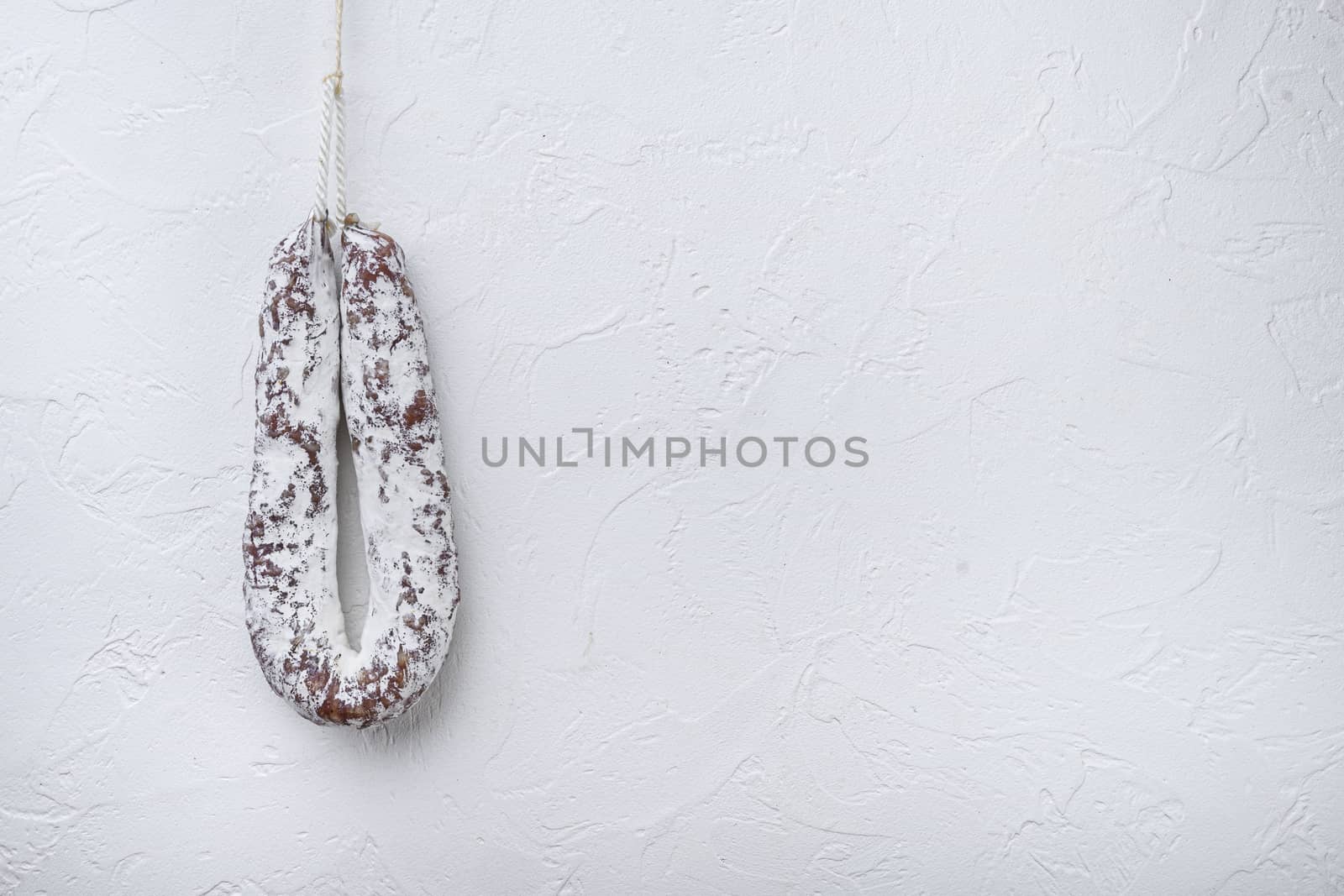 Salami sausage fuet on white textured background with copy space.