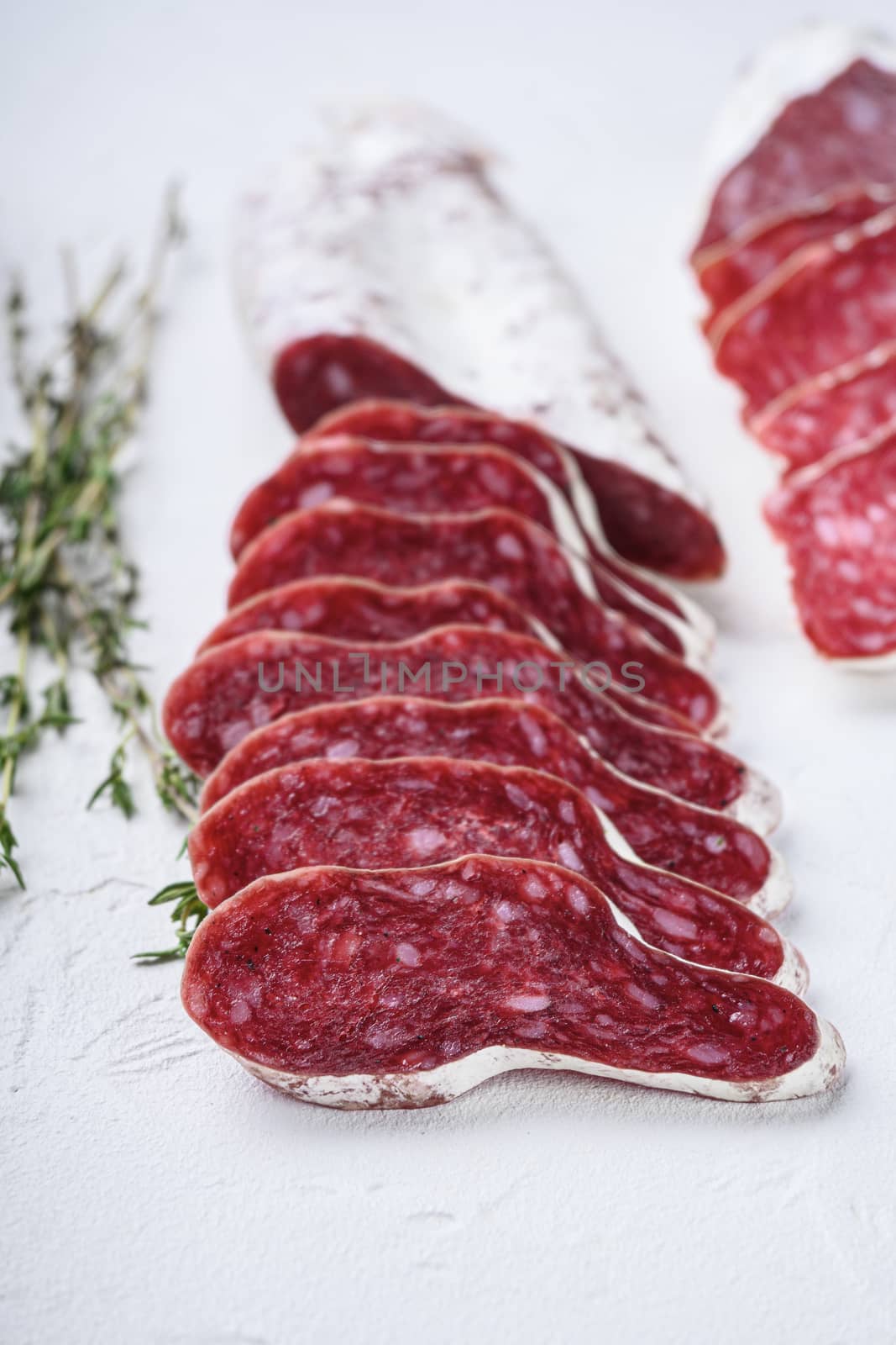 Variety of dry cured fuet and chorizosalami sausages, whole and sliced on white textured background.