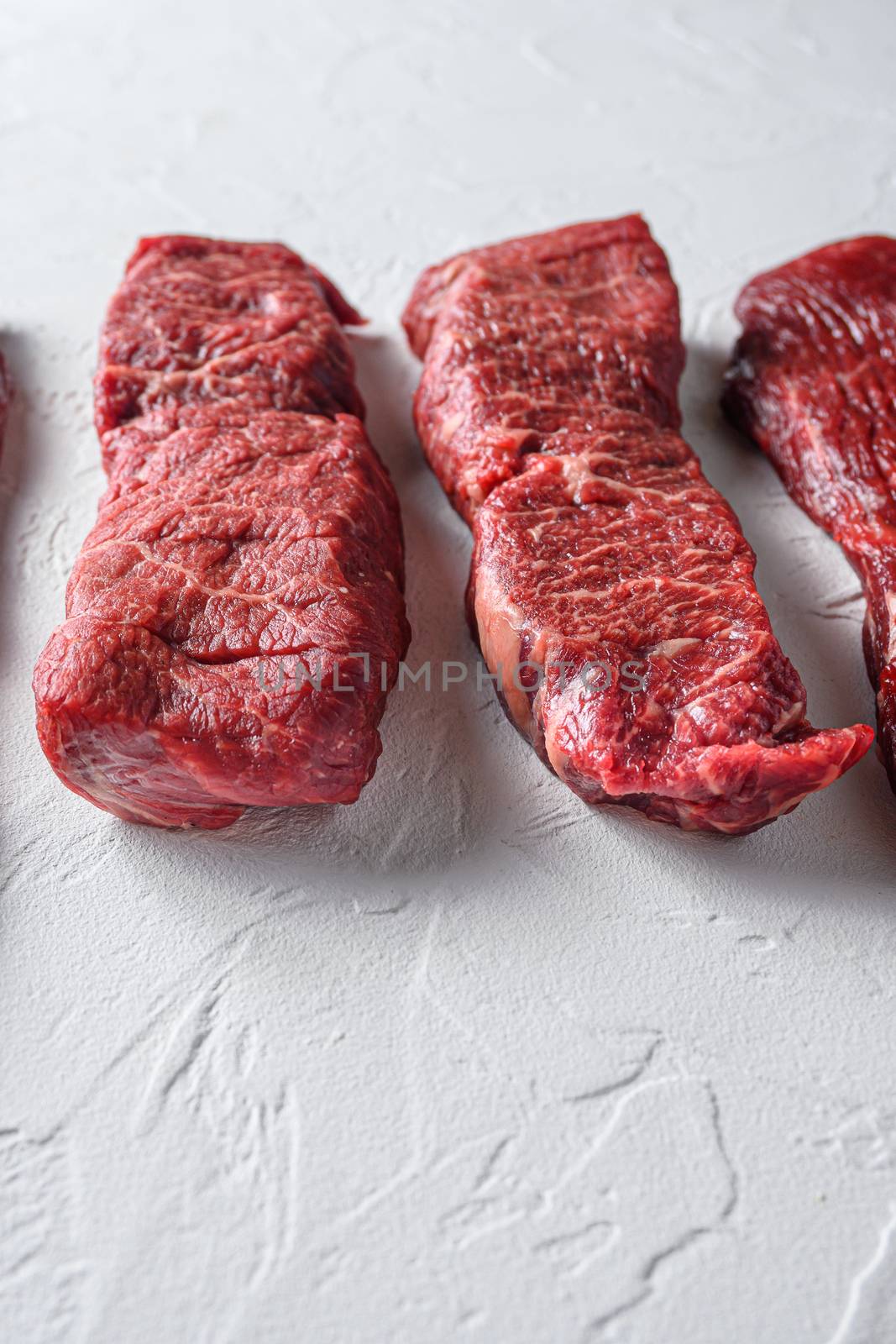 Raw denver steak cut organic meat cut side view close up over white concrete background vertical selective focus.