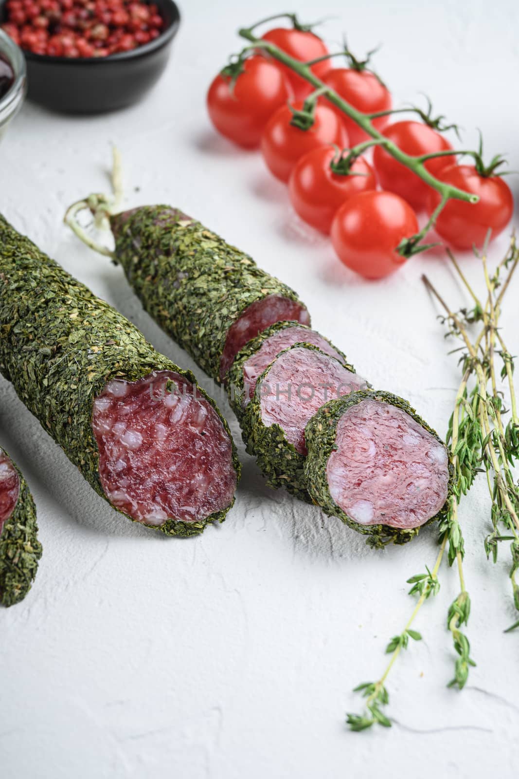 Traditianal fuet sausage in herbs with ingredients on white surface.