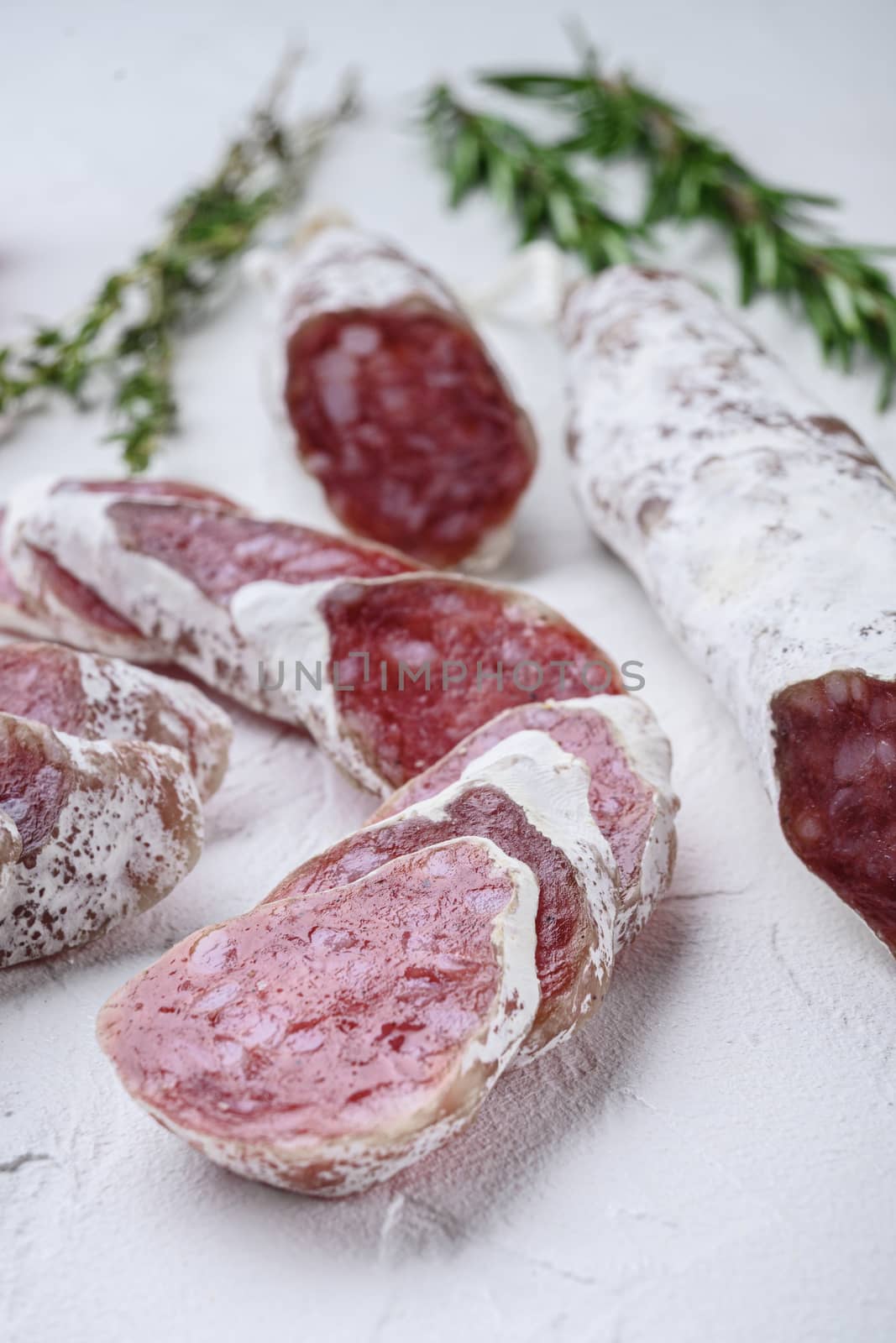 Dry cured fuet salami sausage slices with herbs on white surface.