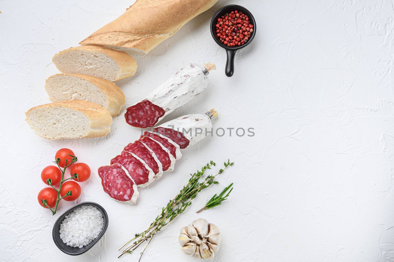 Spanish salcichon slices with panini and herbs on white textured background with space for text.