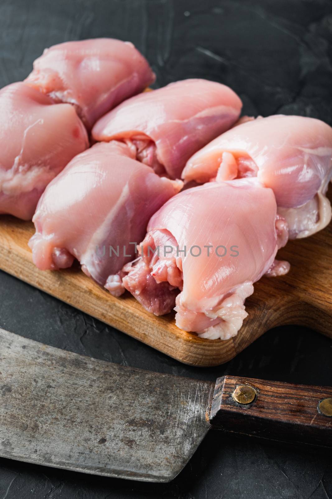 Fresh chicken thighs with meat cleaver, on black background, top view with space for text.