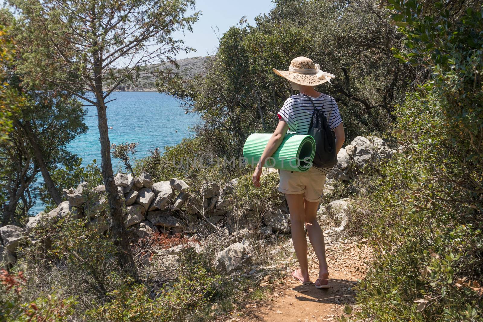 Young active feamle tourist wearing small backpack walking on coastal path among pine trees looking for remote cove to swim alone in peace on seaside in Croatia. Travel and adventure concept by kasto