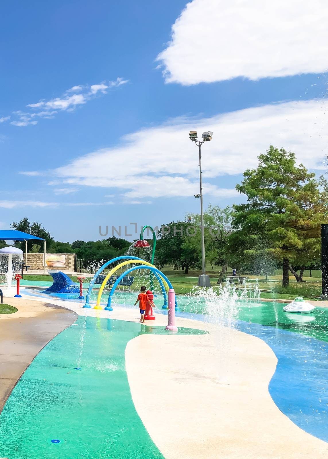 Colorful splash pad water playground with Asian toddler boy playing near Dallas, Texas, America by trongnguyen