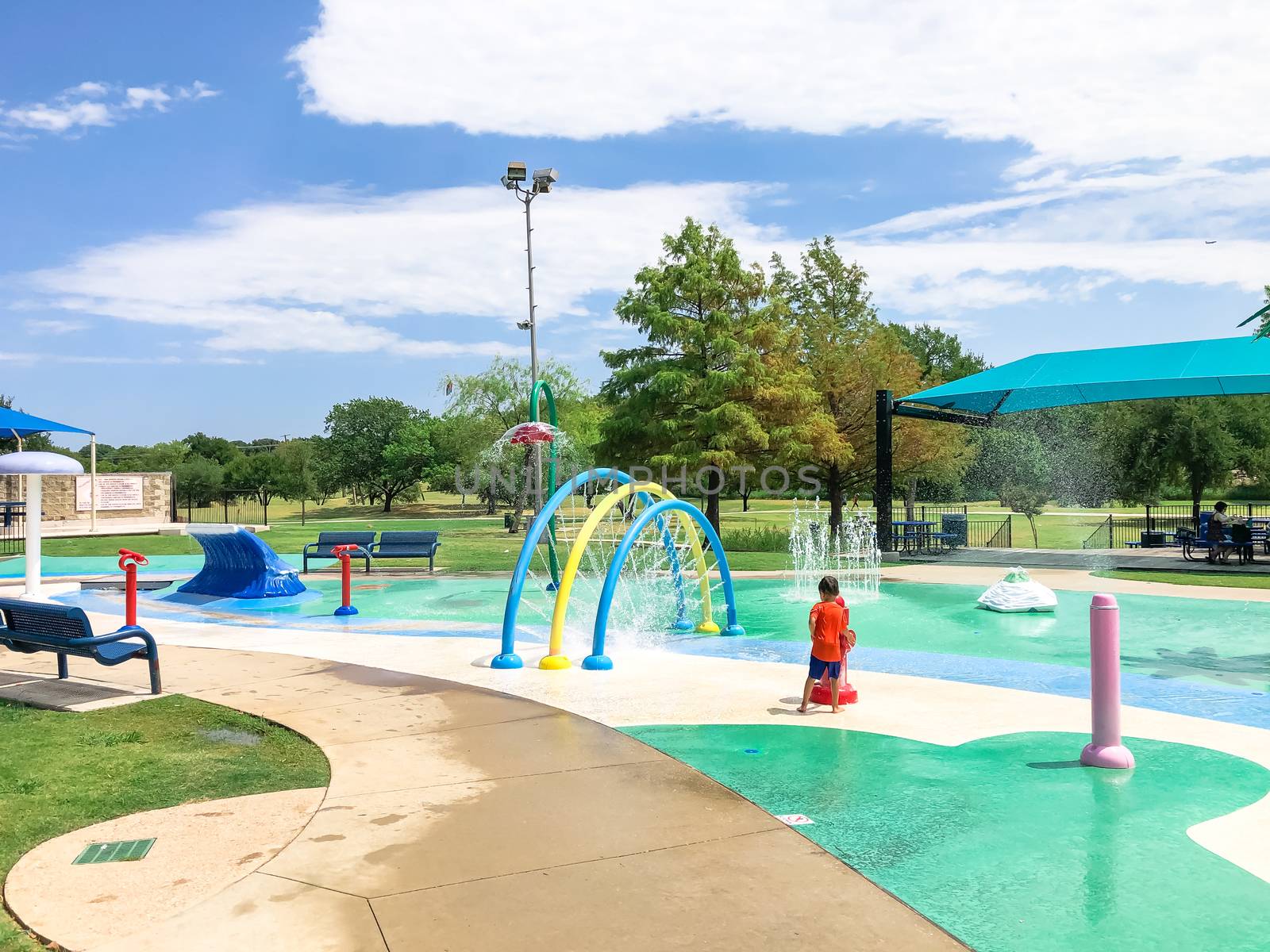 Colorful splash pad water playground with Asian toddler boy playing near Dallas, Texas, America by trongnguyen